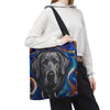 A person wearing a white cropped hoodie and black sweatpants carries a canvas tote bag featuring a painted silver Labrador retriever portrait against a swirling blue, orange, and black background.