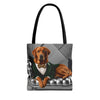 A tote bag with black handles featuring a printed graphic of a fox red Labrador retriever dressed in a green suit and bow tie, sitting on a silver tufted chair against a gray background.