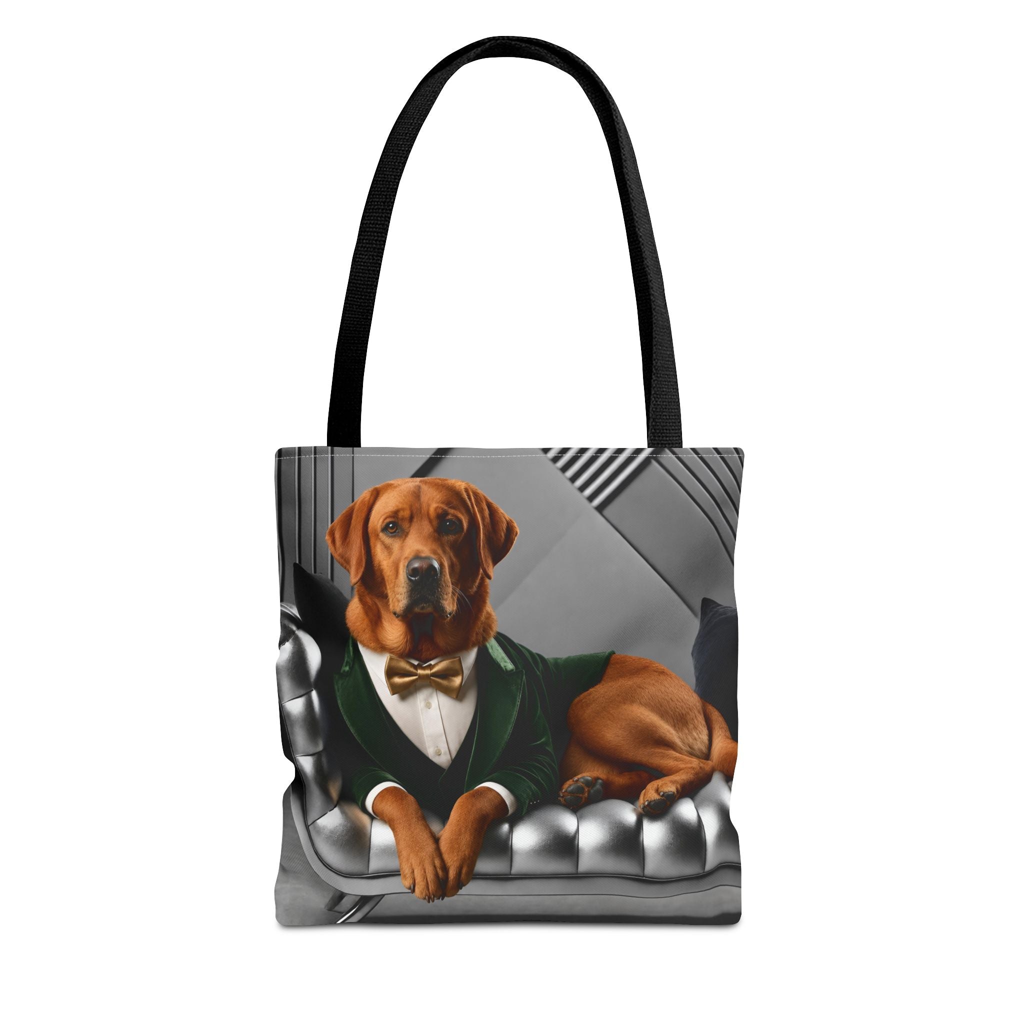 A tote bag with black handles featuring a printed graphic of a fox red Labrador retriever dressed in a green suit and bow tie, sitting on a silver tufted chair against a gray background.