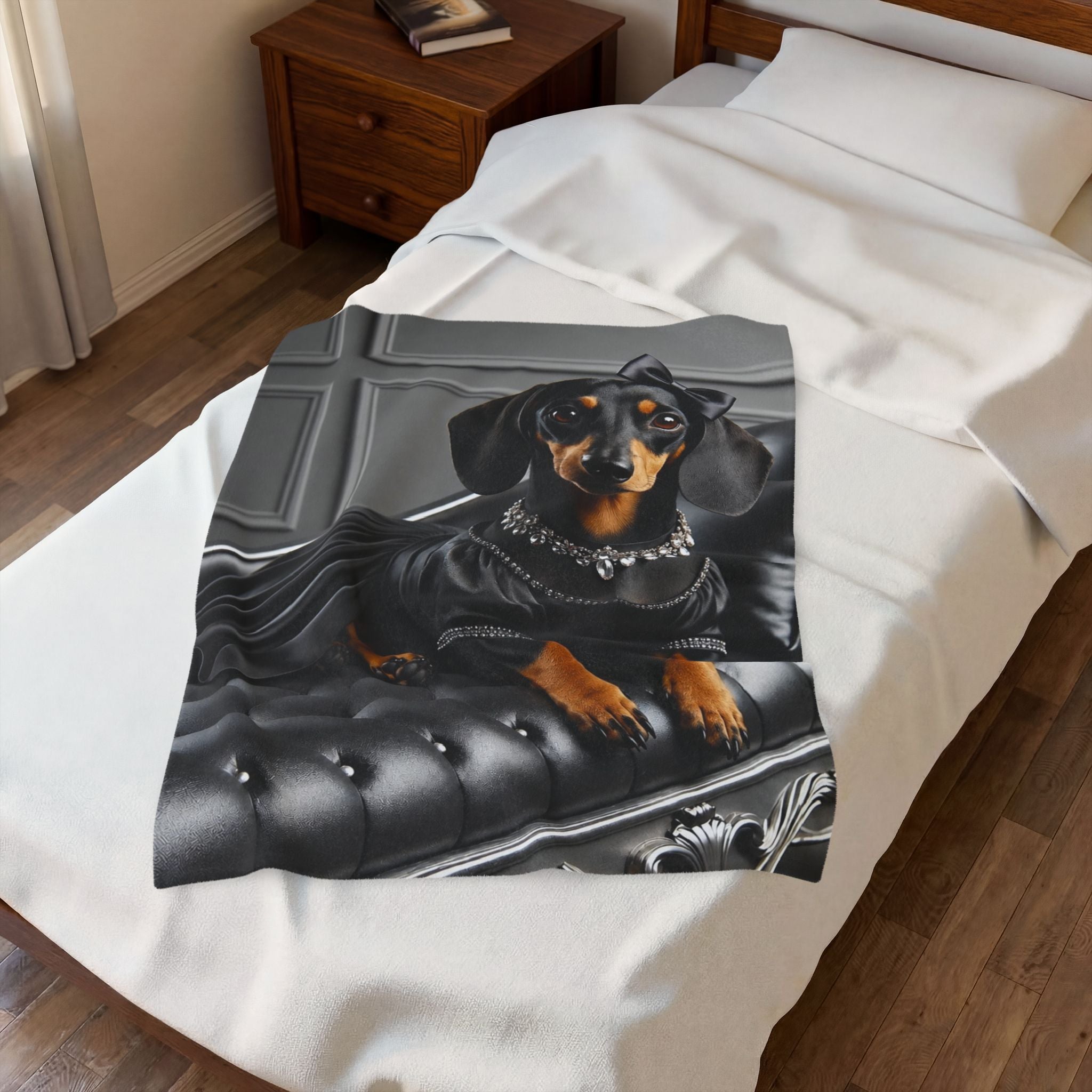 A  blanket featuring a printed portrait of a black and tan dachshund wearing a black dress and silver collar, styled on a bed in a bedroom setting.