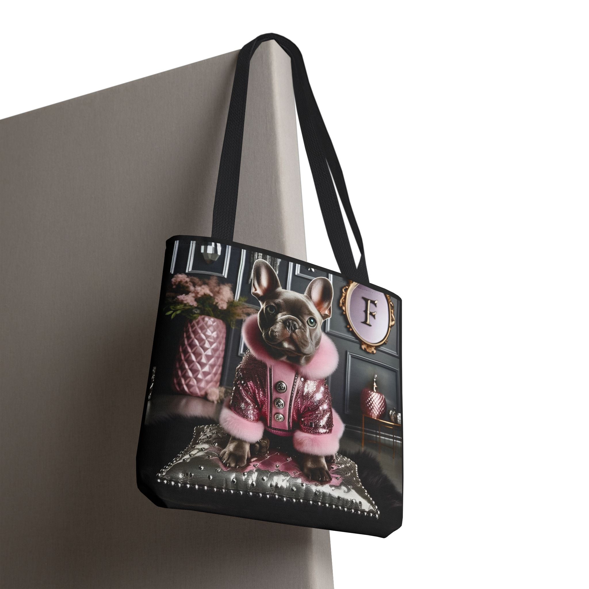A black tote bag with long handles, featuring a printed graphic of a French bulldog dressed in a pink and silver jacket, hanging against a neutral gray background.