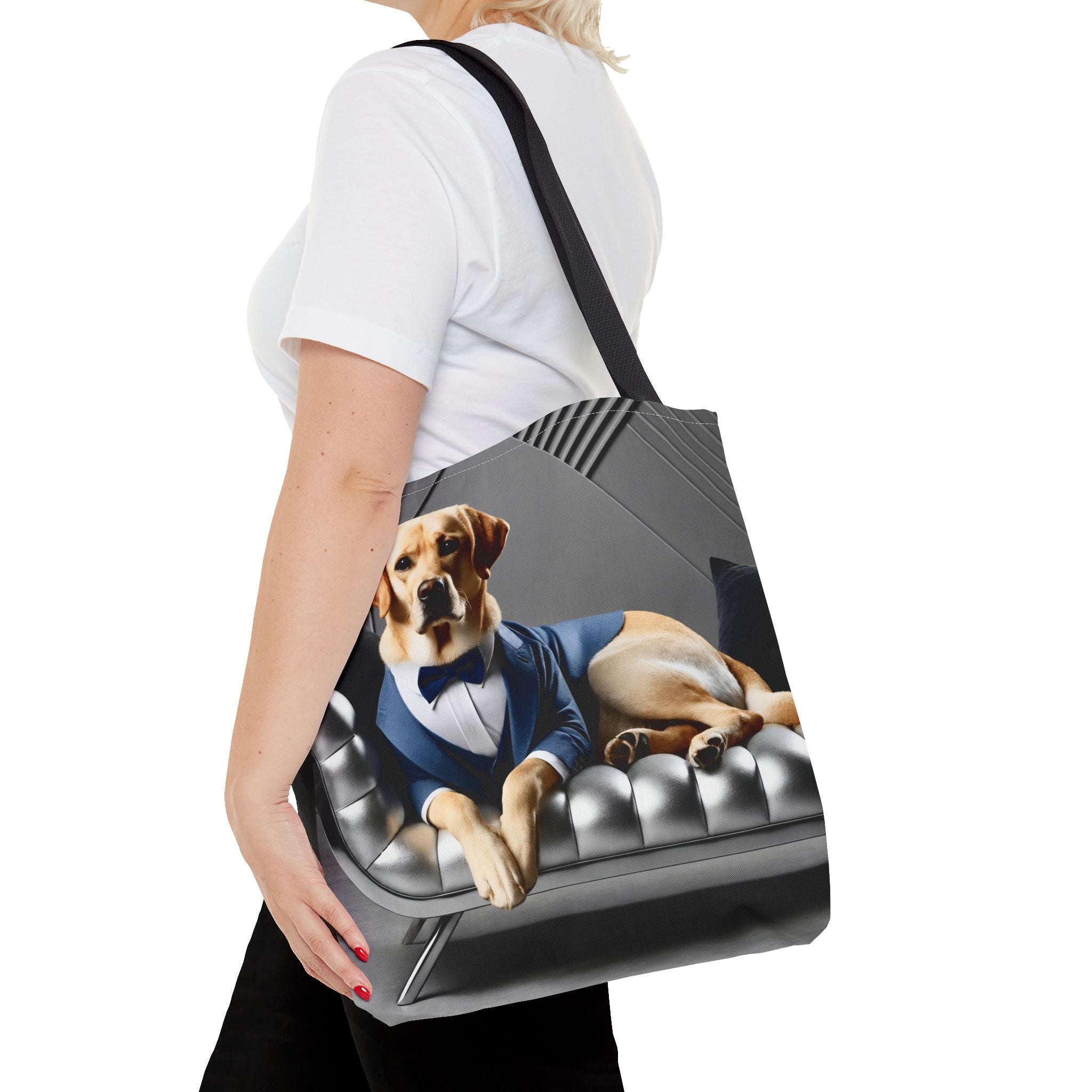 A woman carries a tote bag that features a printed graphic of a yellow Labrador retriever  wearing a blue suit and bow tie, lounging on a tufted gray sofa.