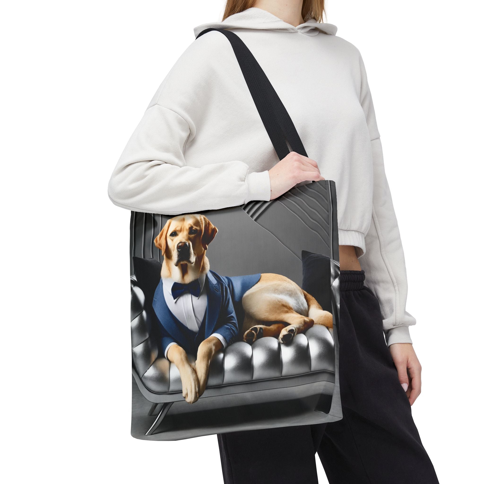 A person carries a large tote bag over their shoulder. The tote bag features a printed graphic of a yellow Labrador retriever dressed in a blue suit and bow tie, lounging on a black tufted leather sofa.