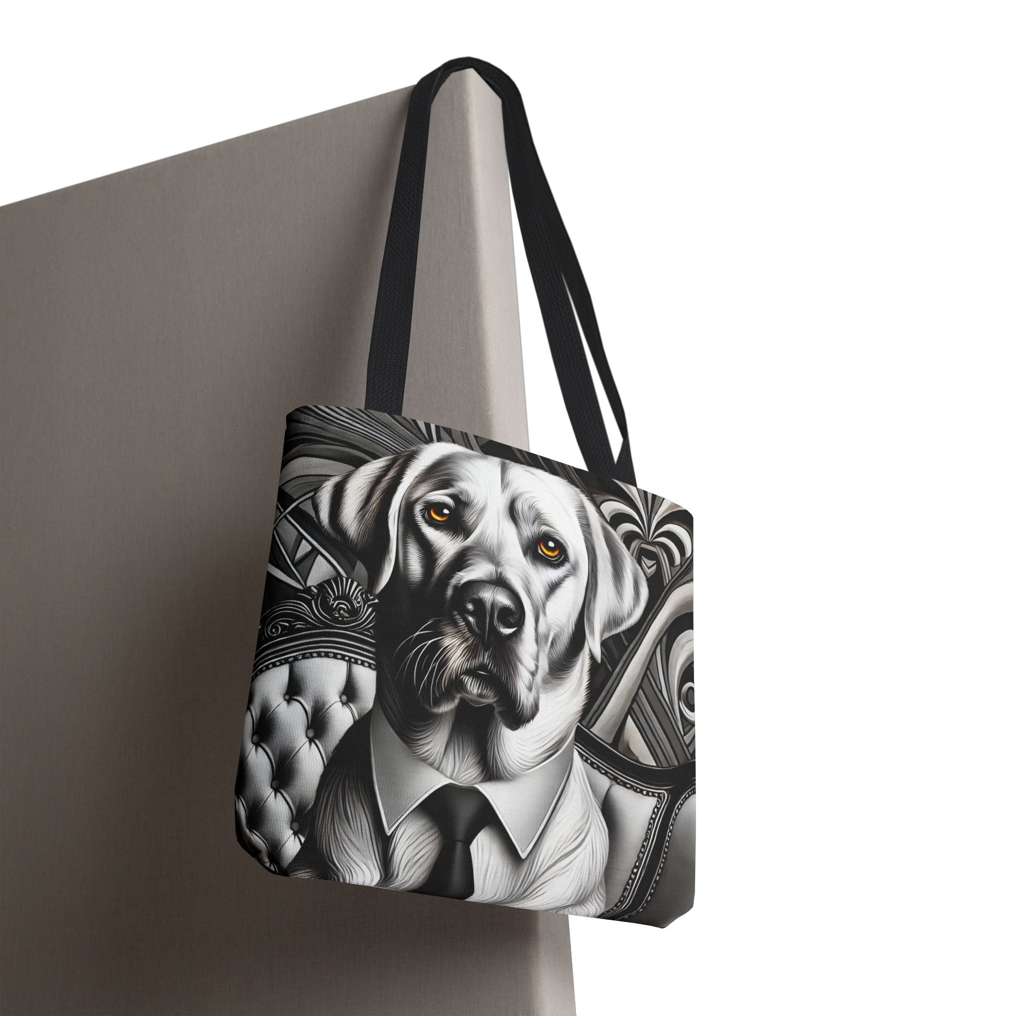A tote bag with black shoulder straps, featuring a black and white graphic illustration of a  Labrador retriever wearing a suit and tie, shown hanging against a neutral gray background.