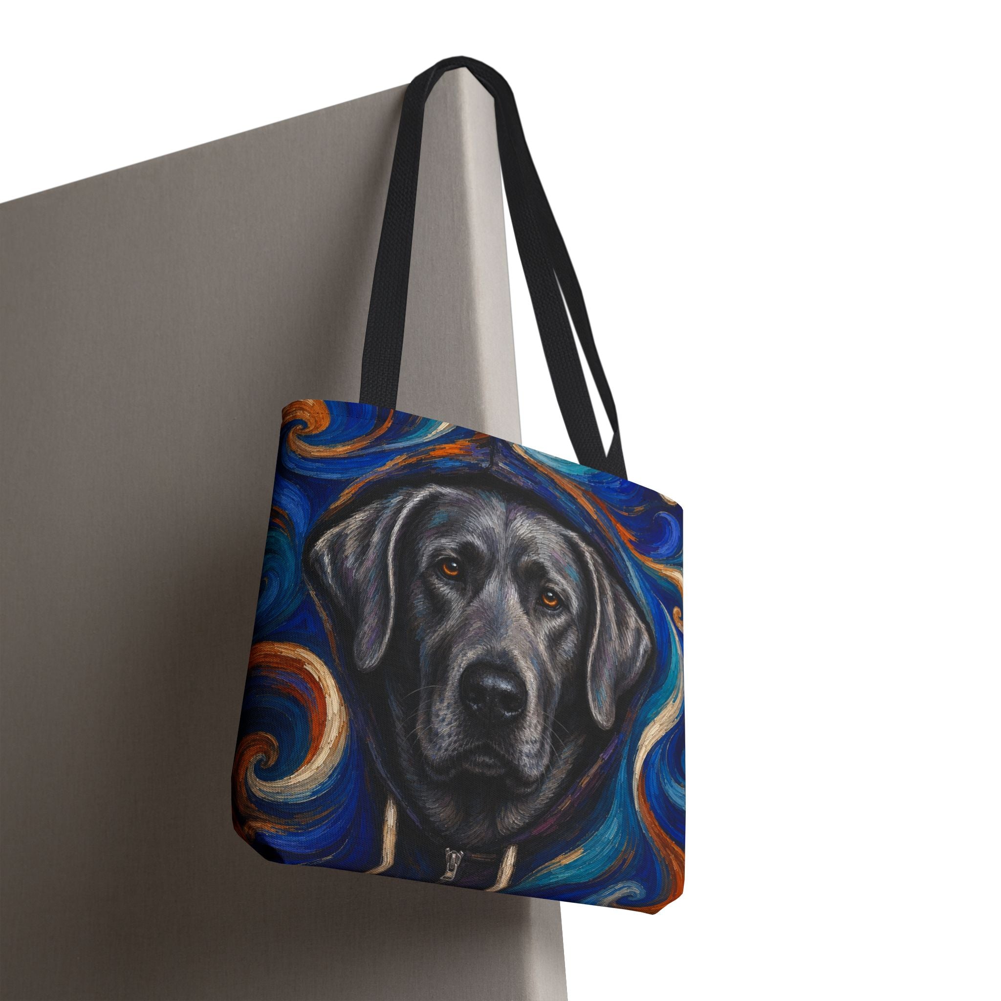 A tote bag with black shoulder straps, featuring a printed illustration of a silver Labrador retriever's face surrounded by swirling blue, orange, and cream artistic patterns, shown hanging against a plain light gray background.