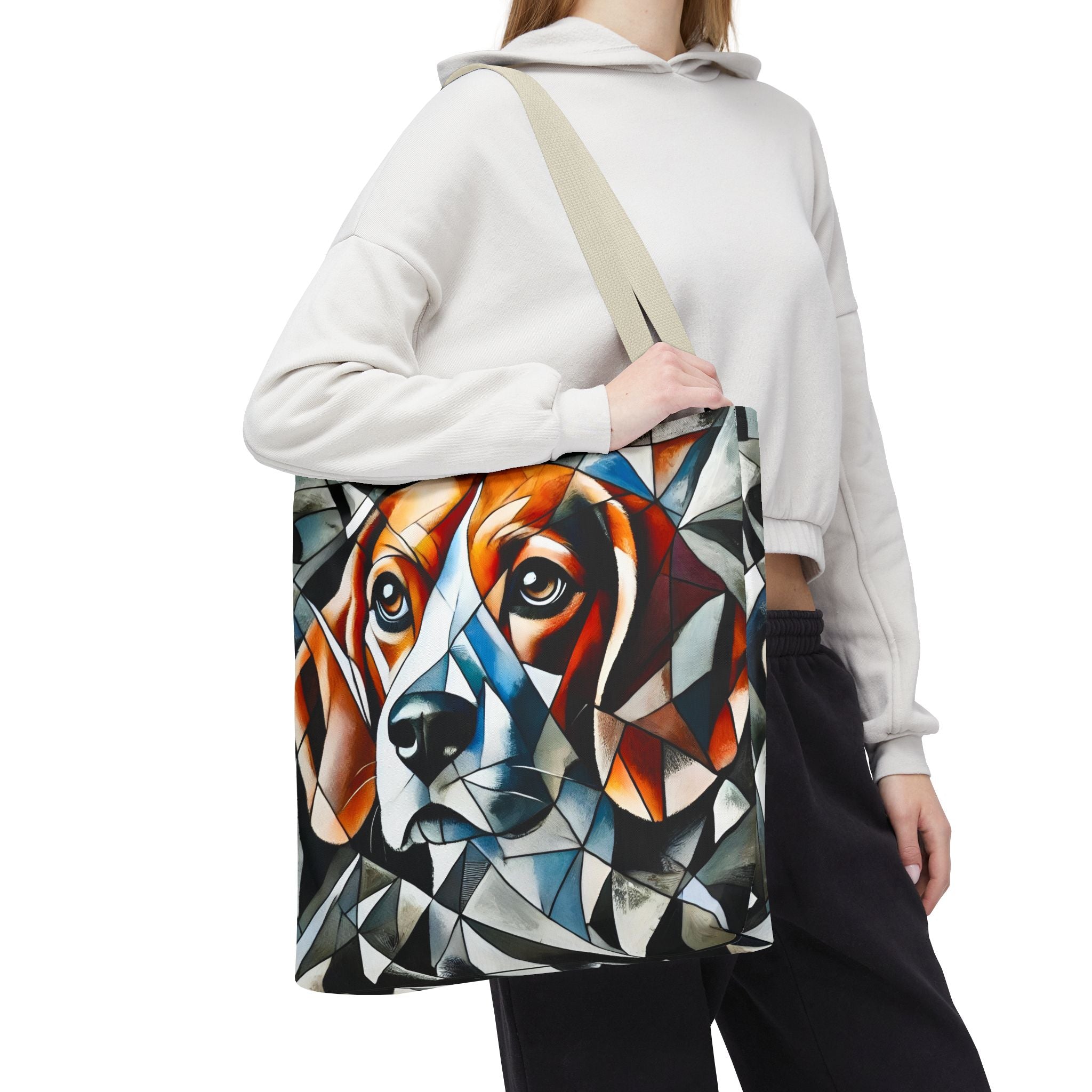 A person wearing a white hoodie and black sweatpants carries a canvas tote bag featuring a colorful geometric beagle dog portrait. The bag has a beige shoulder strap and is shown against a plain white background.