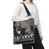 A person carries a large tote bag over their shoulder. The tote bag features a printed graphic of a silver Labrador retriever dressed in a black tuxedo sitting on a tufted gray sofa.