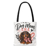 A white canvas tote bag with black shoulder straps, featuring a printed graphic of a dachshund wearing a pink bow, surrounded by the text 'IN MY Dog Mom ERA' with hearts and stars.