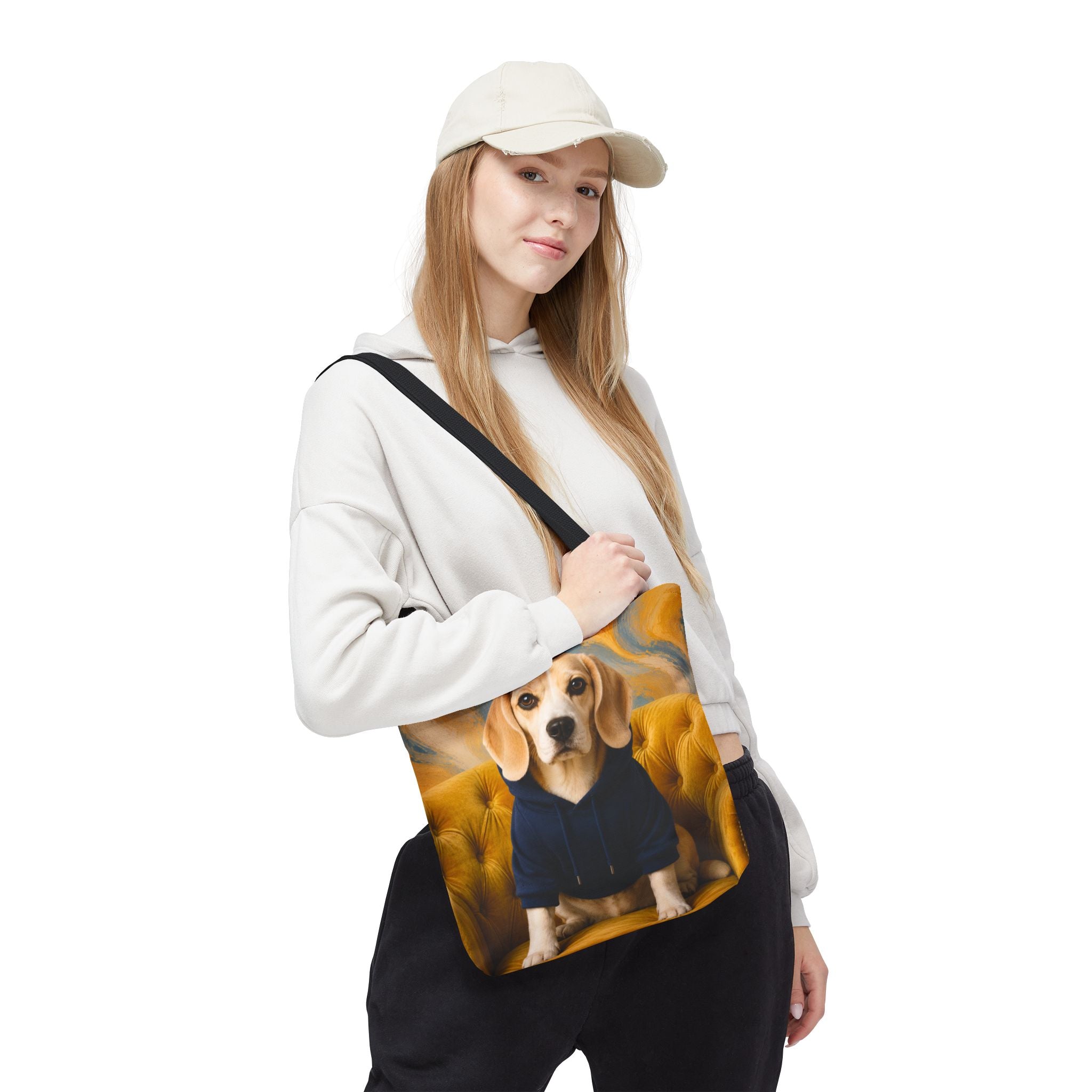 A woman wearing a white hoodie, black sweatpants, and a beige baseball cap carries a canvas tote bag. The bag features a printed graphic of a beagle wearing a blue hoodie against a warm yellow and orange background.