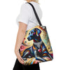 A woman wearing a white t-shirt and black pants carries a colorful tote bag featuring a stylized painting of a black Labrador retriever with a silver collar and a pink heart, set against a plain white background.