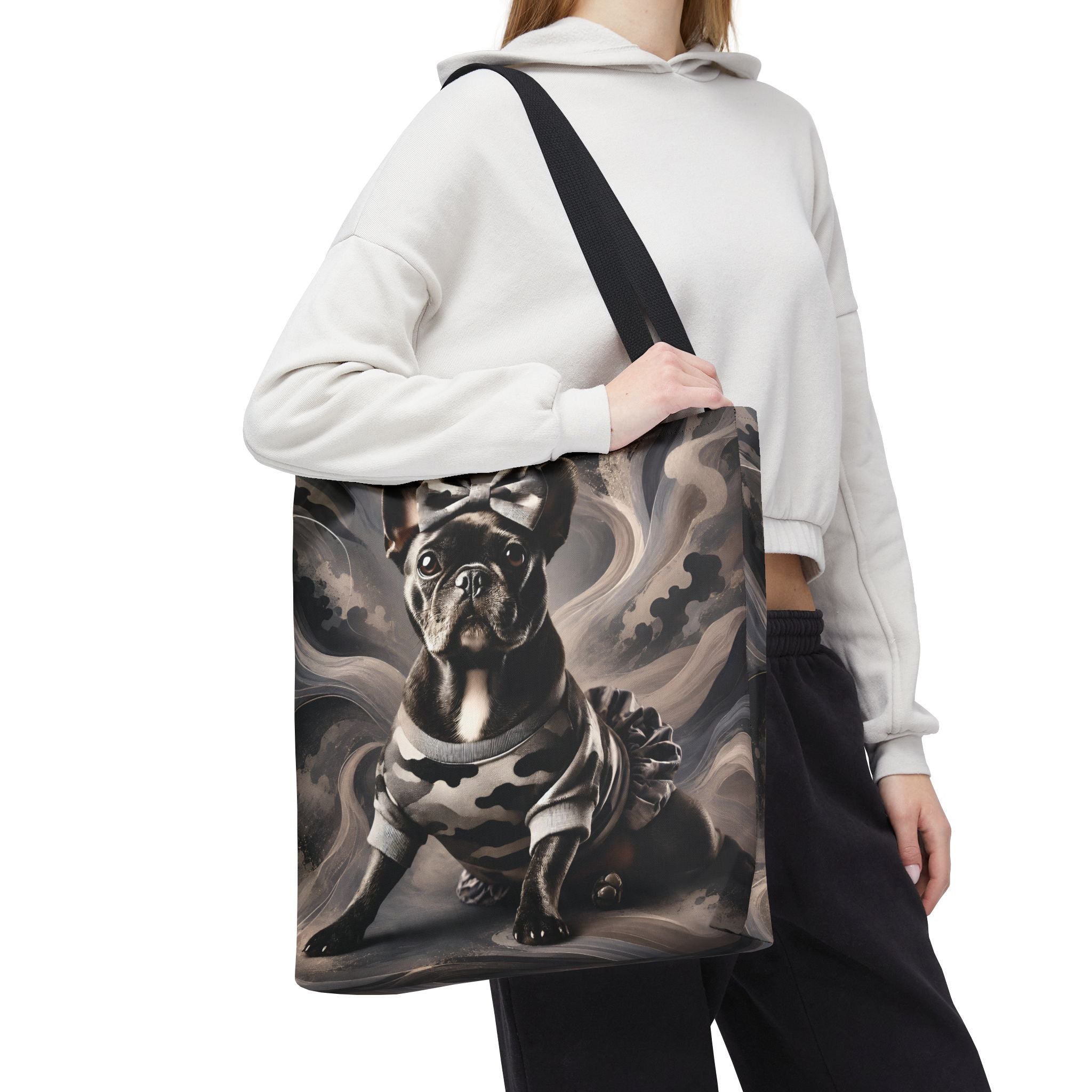 A person wearing a white cropped hoodie and black sweatpants carries a large tote bag with a printed illustration of a black French bulldog on a smoky gray background. The bag has a black shoulder strap and is shown against a plain white studio background.