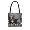 A tote bag with black handles, featuring a printed graphic of a silver Labrador retriever dressed in a red tuxedo jacket, white shirt, and black bow tie, sitting on a tufted gray sofa.