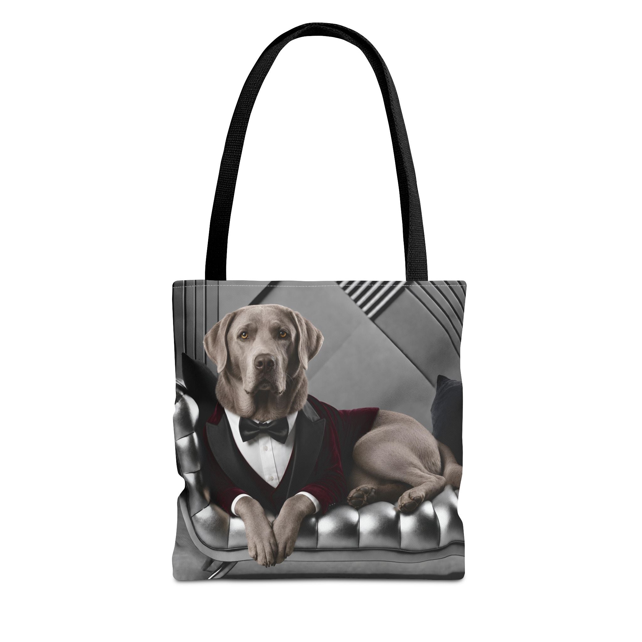A tote bag with black handles, featuring a printed graphic of a silver Labrador retriever dressed in a red tuxedo jacket, white shirt, and black bow tie, sitting on a tufted gray sofa.