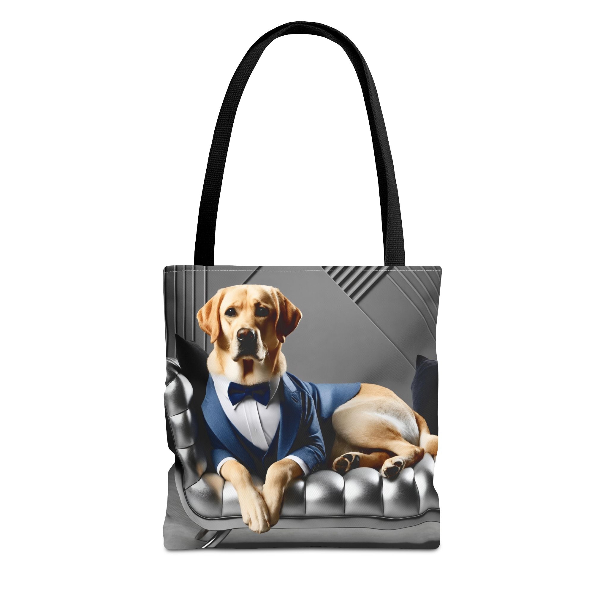 A tote bag with black handles featuring a printed graphic of a yellow Labrador retriever dog dressed in a blue suit and bow tie, lying on a gray tufted sofa.