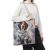 A person wearing a white cropped hoodie and black sweatpants carries a canvas tote bag with a printed illustration of a beagle dog in a blue camouflage hoodie against a swirling blue and gray background.