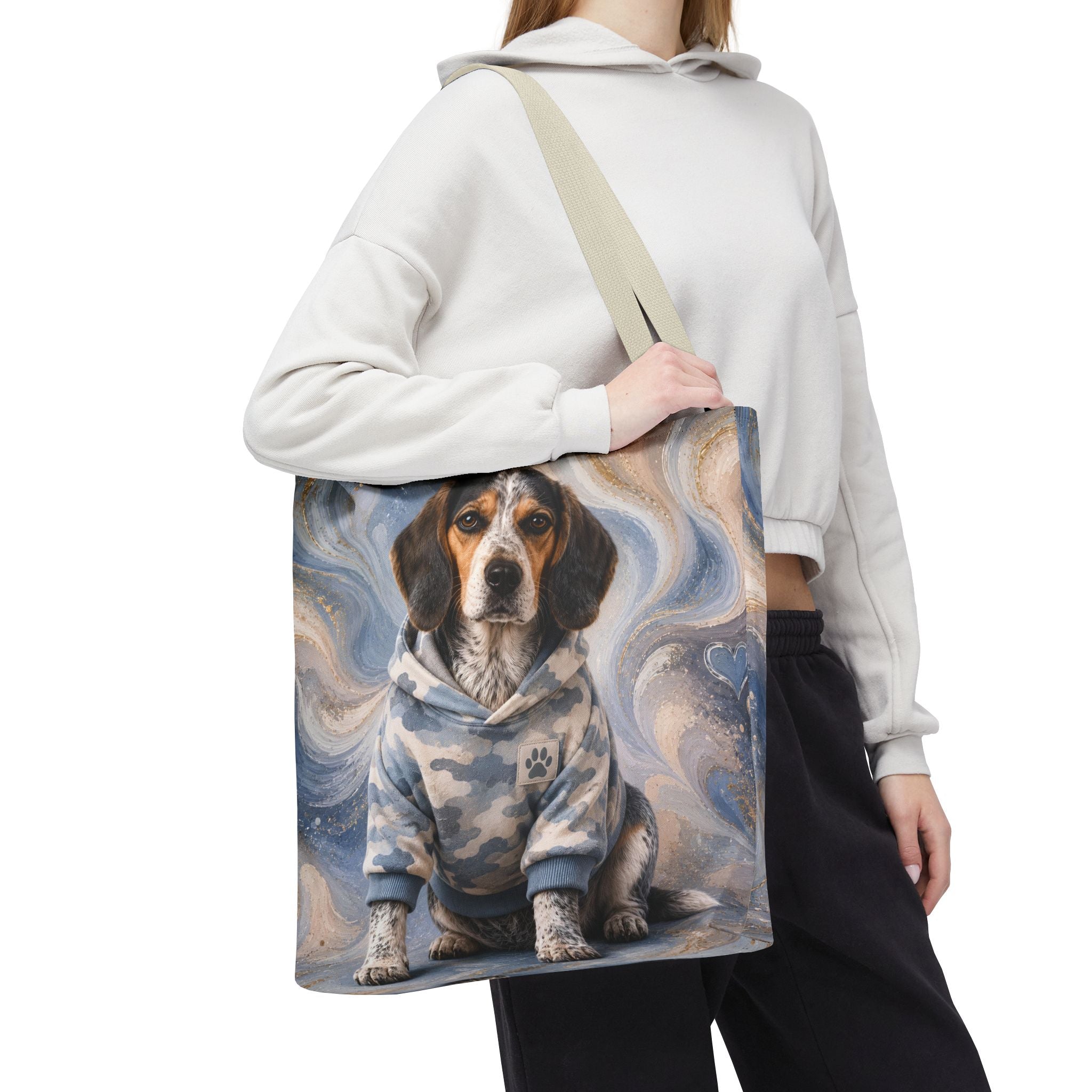 A person wearing a white cropped hoodie and black sweatpants carries a canvas tote bag with a printed illustration of a beagle dog in a blue camouflage hoodie against a swirling blue and gray background.