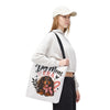 A woman wearing a white cap, white sweatshirt, and black pants carries a white canvas tote bag with a black strap. The bag features a graphic of a dachshund wearing a pink bow, with the text 'Dog Mom ERA' in black and pink lettering.