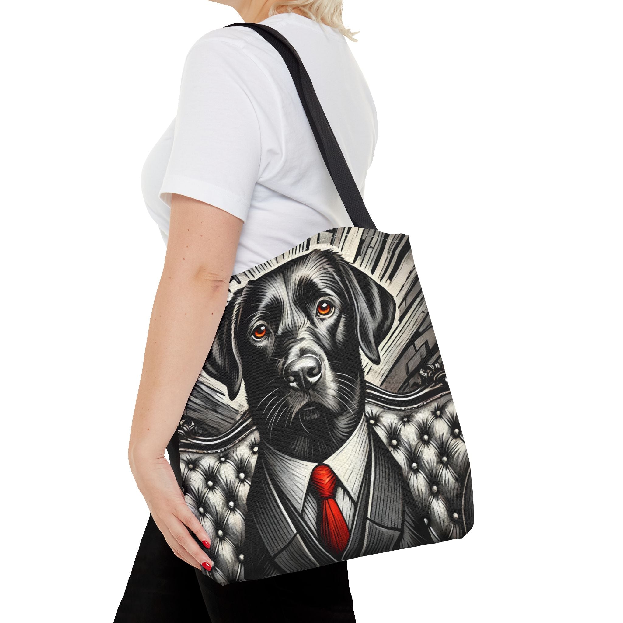 A woman wearing a white t-shirt and black pants carries a black shoulder tote bag featuring a graphic print of a black Labrador dog dressed in a suit and red tie, set against a clean white background.
