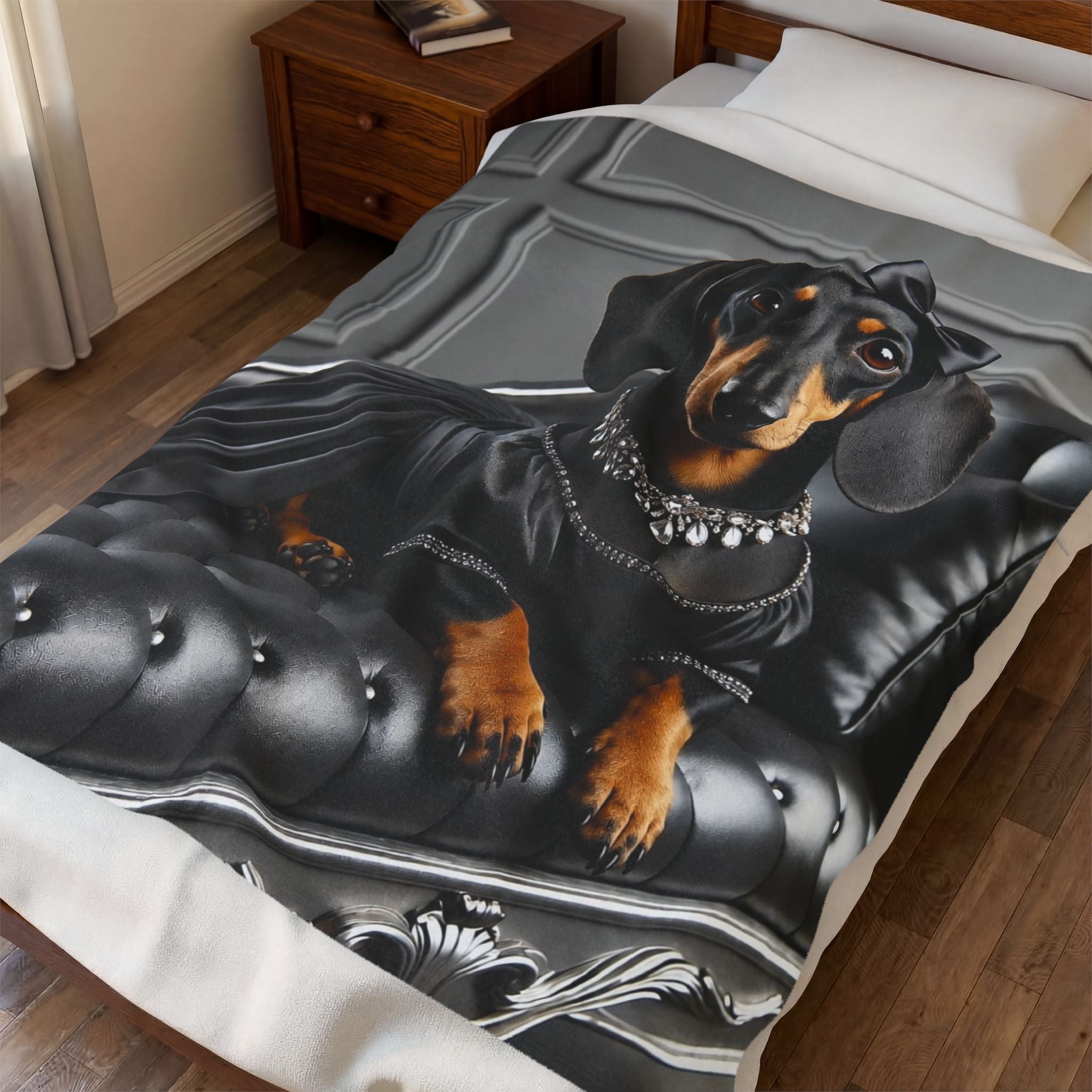 A printed blanket or comforter spread across a bed, featuring a realistic portrait of a black and tan dachshund wearing a silver collar, set against a gray tufted sofa. The bedding is styled in a bedroom with a wooden nightstand and wood floor.
