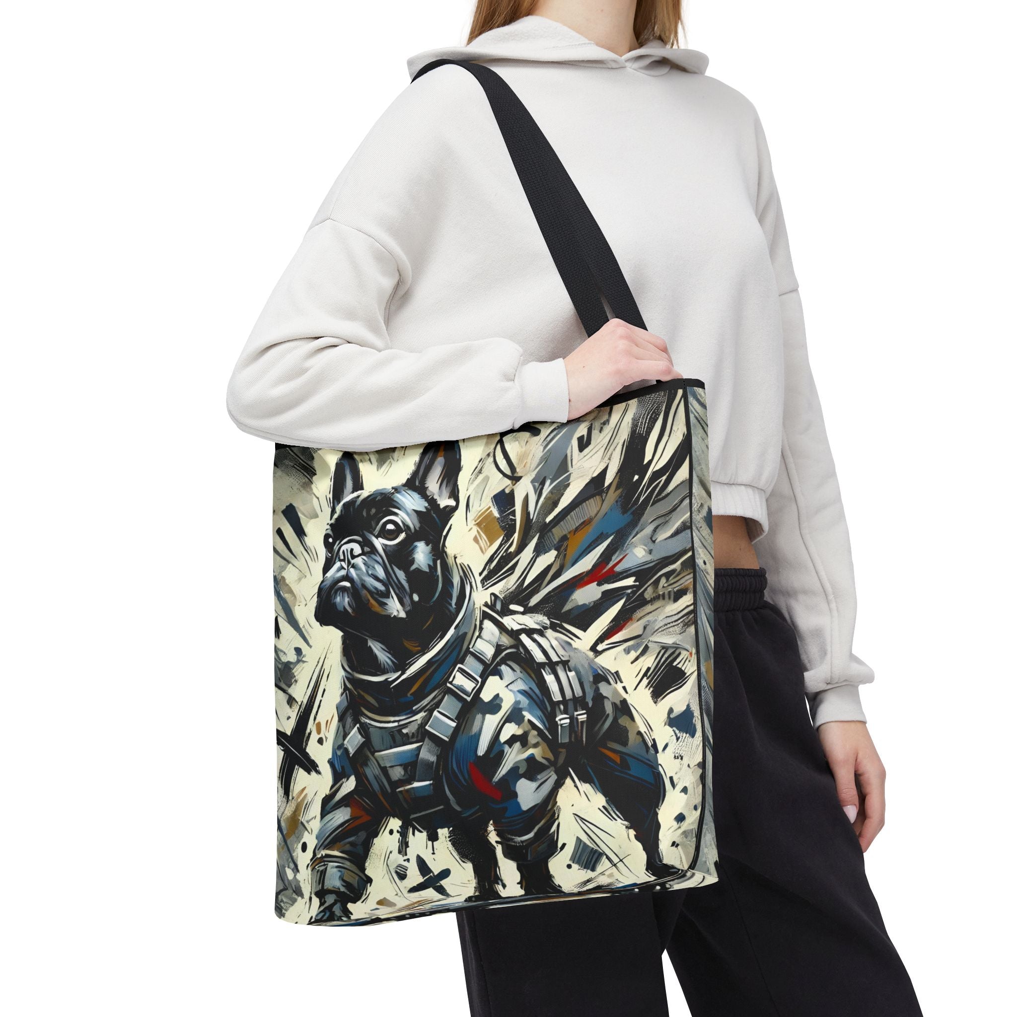 A person wearing a white hoodie and black sweatpants carries a large tote bag with a printed illustration of a black French bulldog in a tactical armor. The background is solid white.