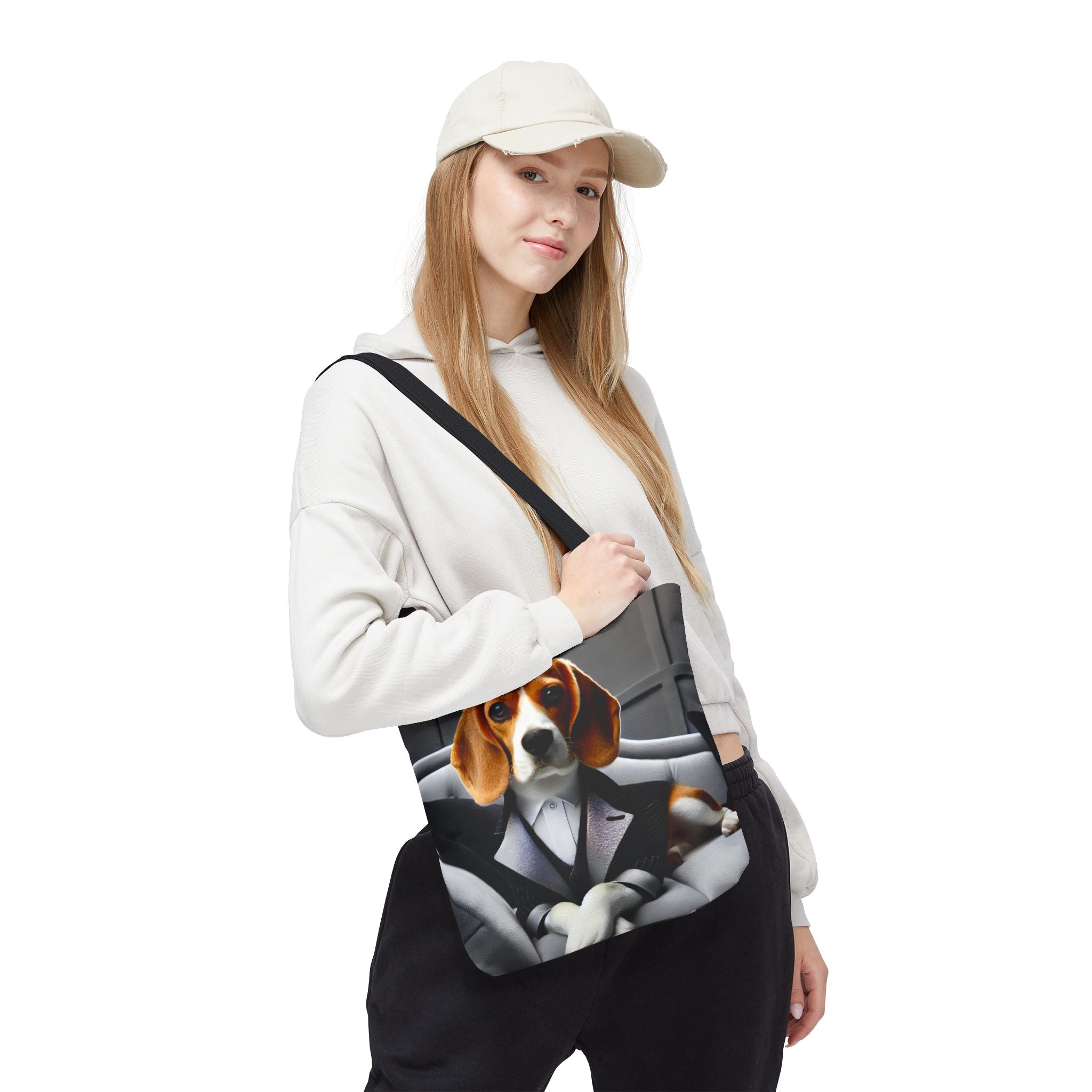 A woman wearing a beige cap, white hoodie, and black sweatpants carries a black shoulder tote bag featuring a printed graphic of a beagle dog in a suit sitting in a car.