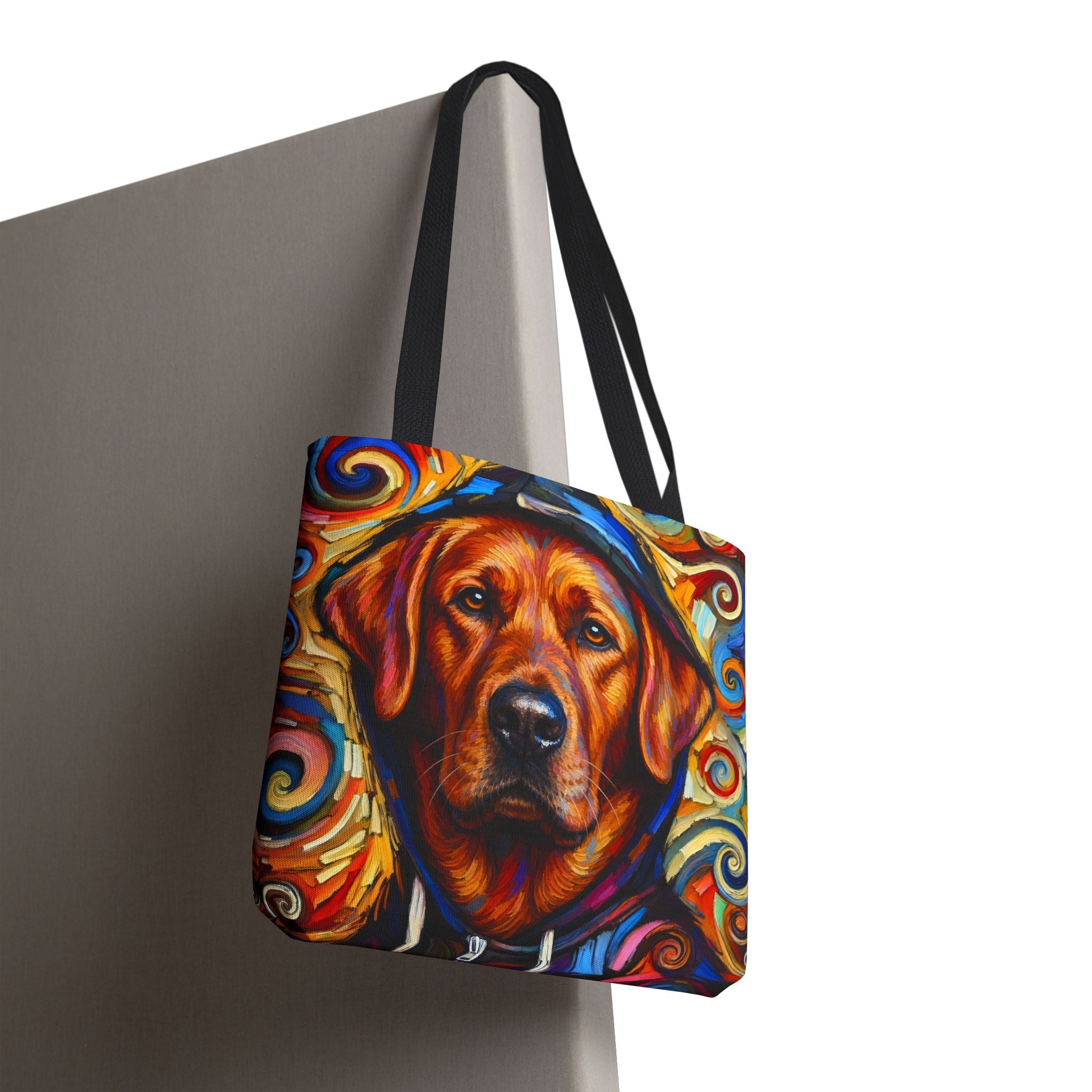 A tote bag with black shoulder straps, featuring a colorful artistic print of a red fox Labrador Retriever wearing a hat, shown hanging against a gray wall on a white background.