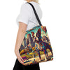 A woman wearing a white t-shirt and black pants carries a canvas tote bag over her shoulder. The bag features a vibrant, colorful graphic print of a Boston Terrier dog in a stylized city park setting with swirling patterns.