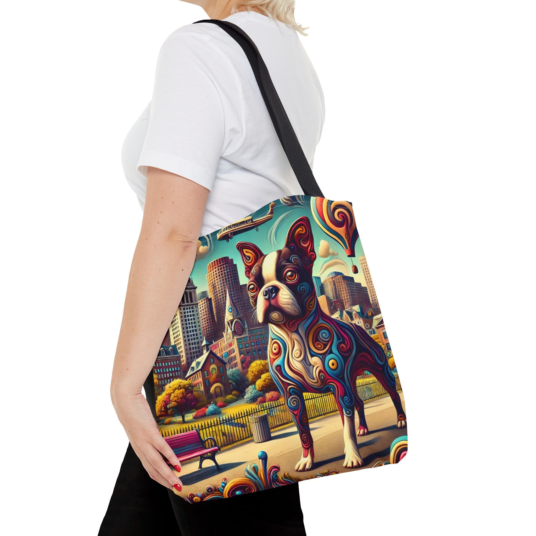 A woman wearing a white t-shirt and black pants carries a canvas tote bag over her shoulder. The bag features a vibrant, colorful graphic print of a Boston Terrier dog in a stylized city park setting with swirling patterns.
