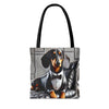 A tote bag with black shoulder straps, featuring a printed graphic of a dachshund dressed in a black tuxedo and bow tie, sitting on a gray tufted chair against a light gray background.