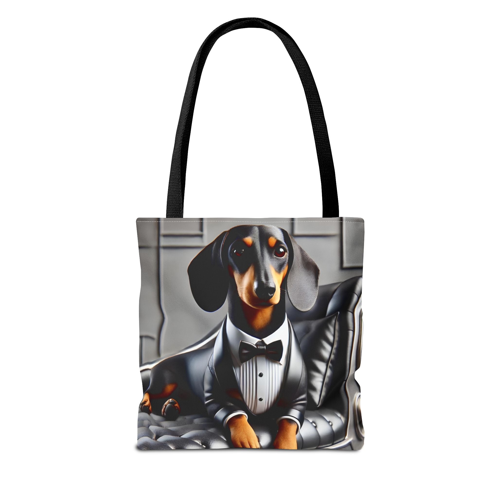 A tote bag with black shoulder straps, featuring a printed graphic of a dachshund dressed in a black tuxedo and bow tie, sitting on a gray tufted chair against a light gray background.