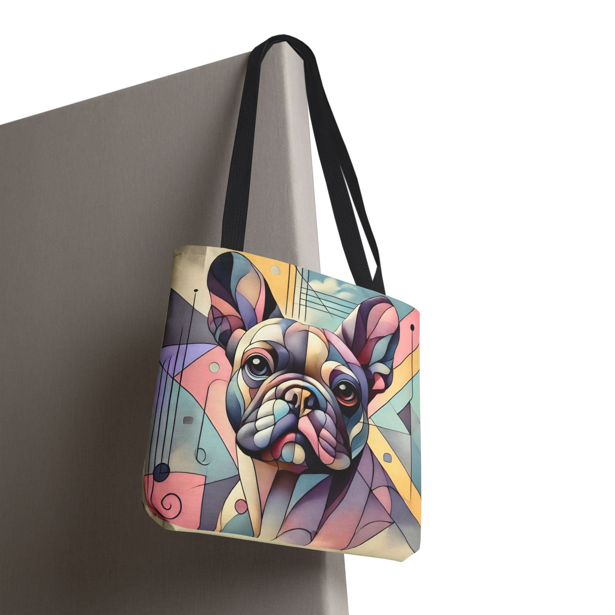 A tote bag with black shoulder straps, featuring a colorful geometric illustration of a French Bulldog on the front, shown hanging against a neutral gray background.