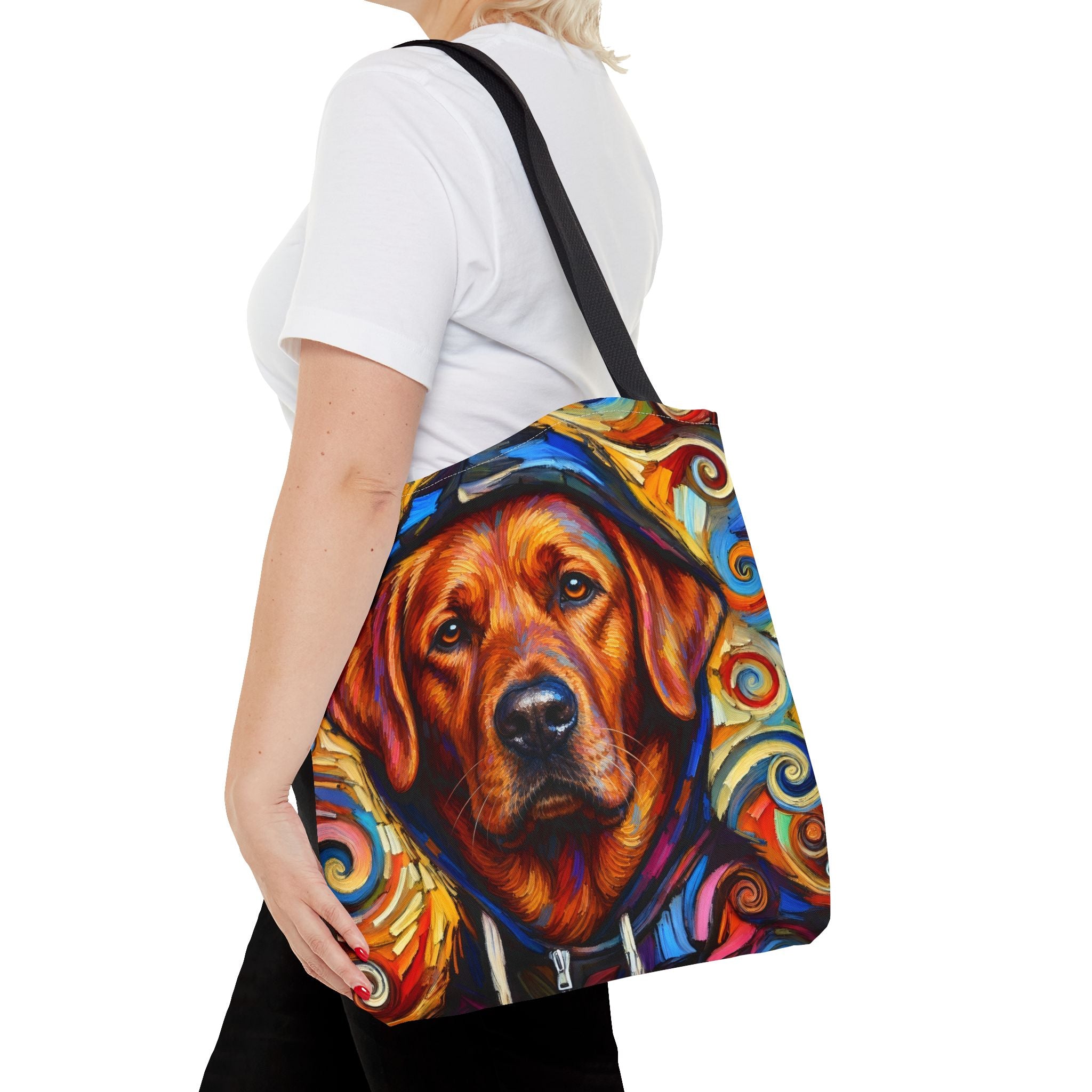A woman wearing a white t-shirt and black pants carries a colorful tote bag featuring a stylized portrait of a red fox Labrador Retriever dog in a hoodie, set against a plain white background.