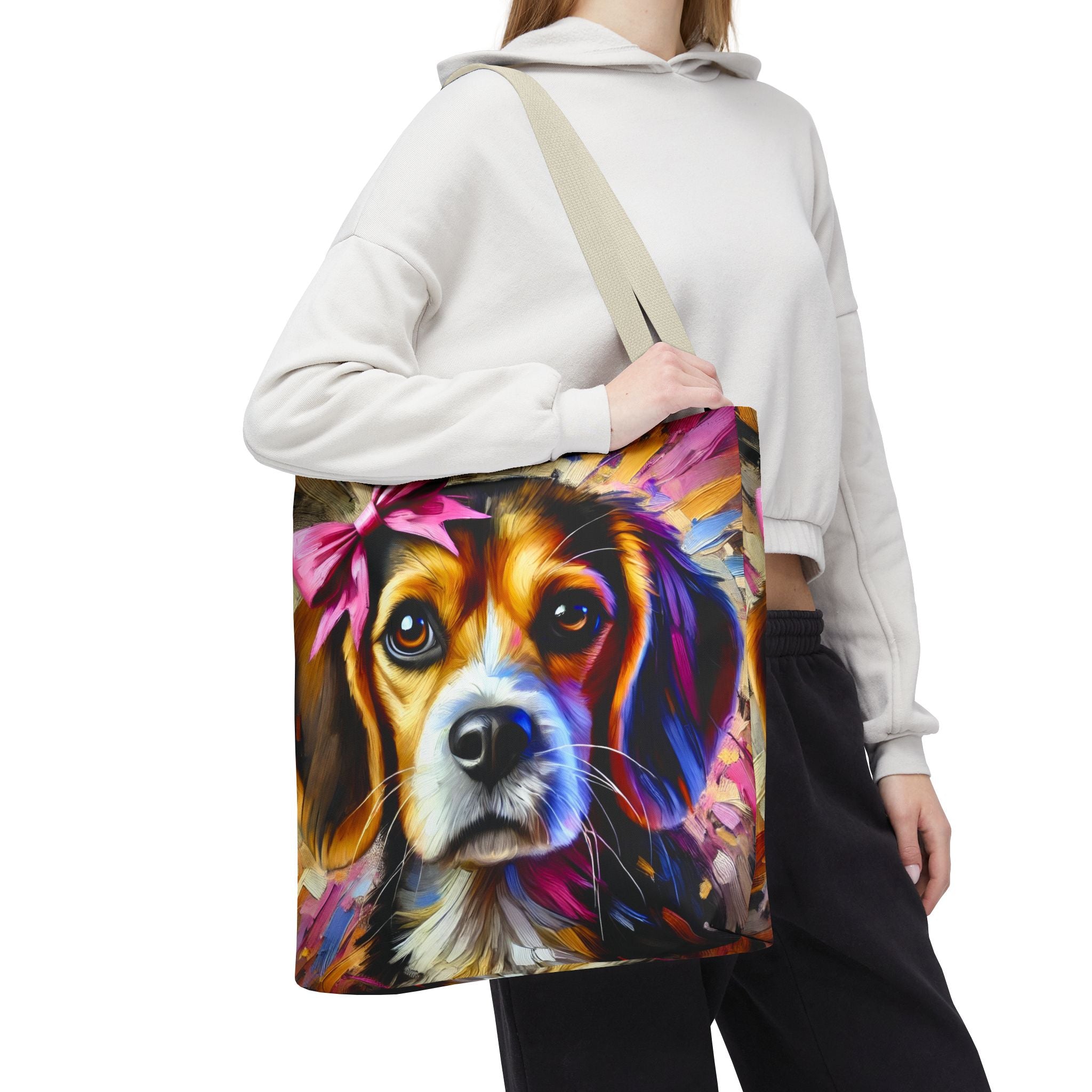 A person wearing a white cropped hoodie and black sweatpants carries a large canvas tote bag over their shoulder. The bag features a colorful, painterly portrait of a beagle with a pink bow on a plain white background.