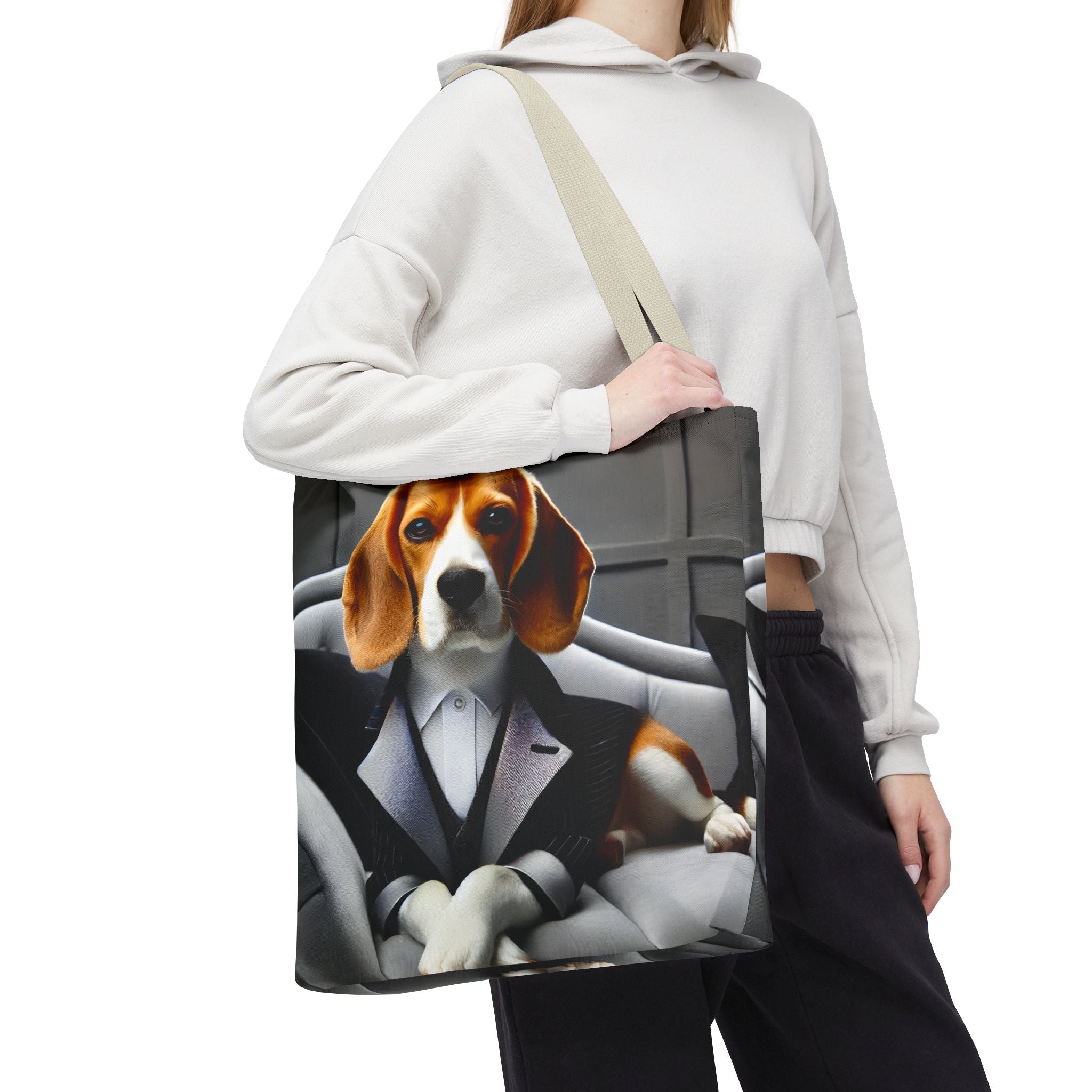 A person wearing a white hoodie and black sweatpants carries a canvas tote bag over their shoulder. The bag features a printed graphic of a beagle dog dressed in a black tuxedo and bow tie sitting in a gray car interior.