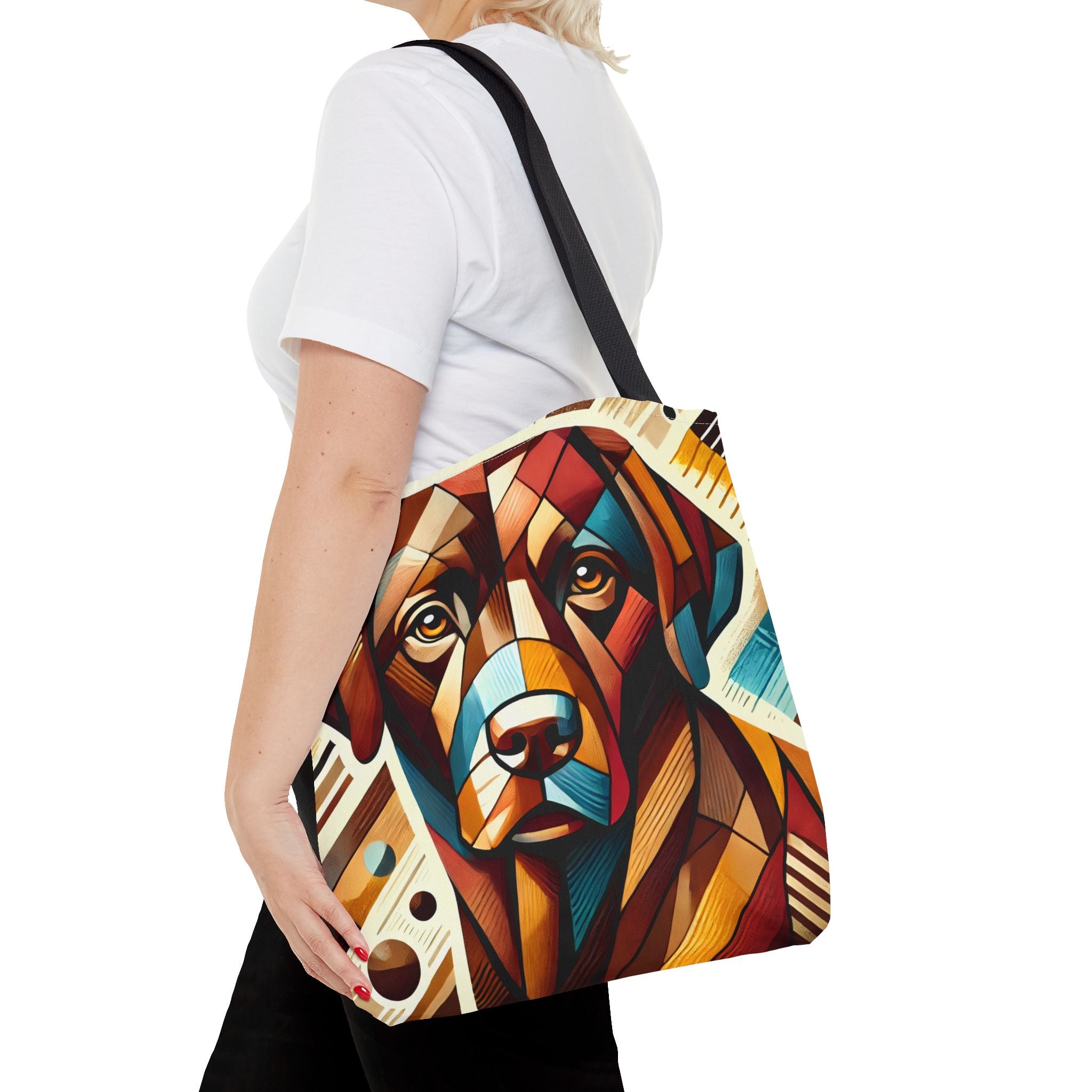A woman carries a canvas tote bag featuring a colorful geometric chocolate Labrador retriever portrait. The bag has a black shoulder strap.