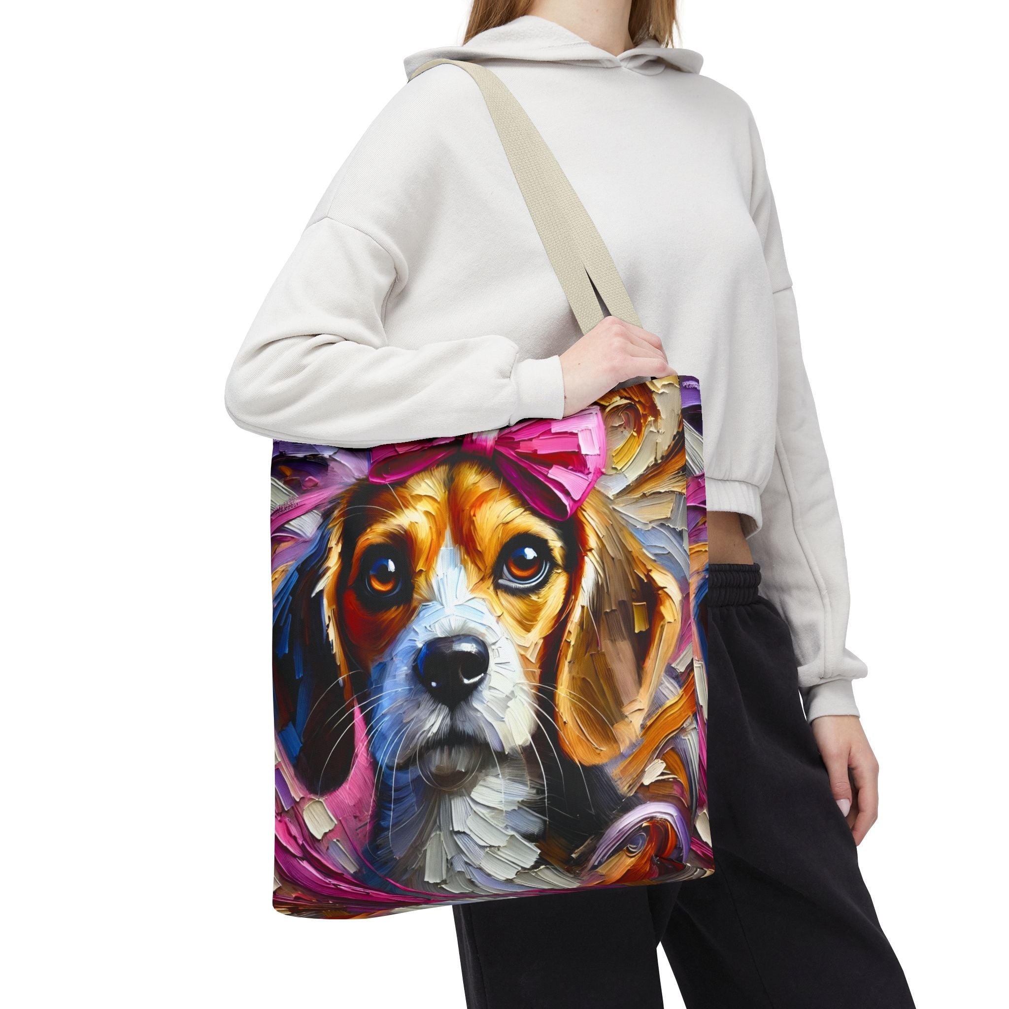 A person wearing a white cropped hoodie and black sweatpants carries a canvas tote bag with a colorful painted beagle dog design on the front. The bag has a beige shoulder strap and is shown against a plain white background.