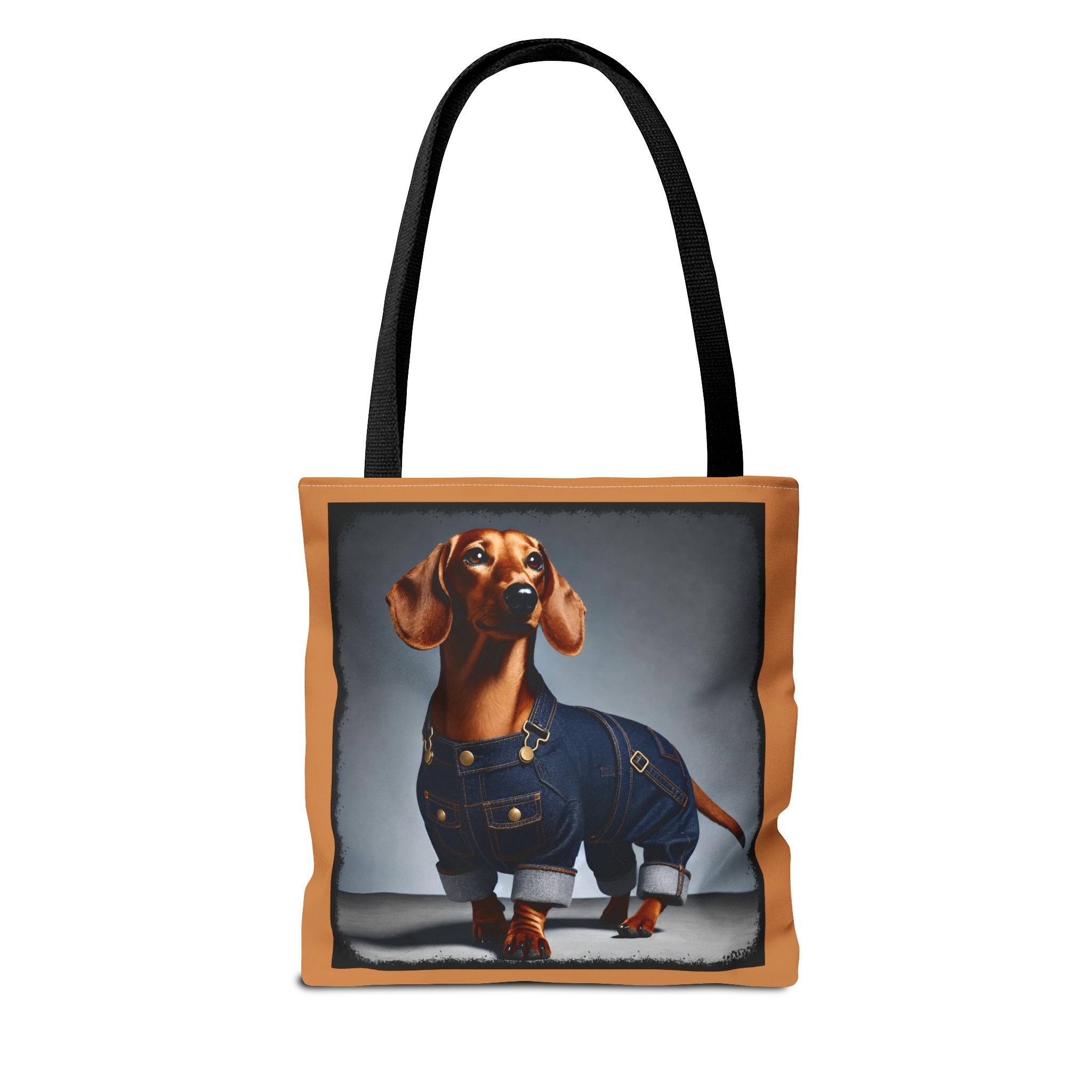 A tote bag with black shoulder straps and a tan border, featuring a printed graphic of a dachshund wearing blue denim overalls against a gray studio background.