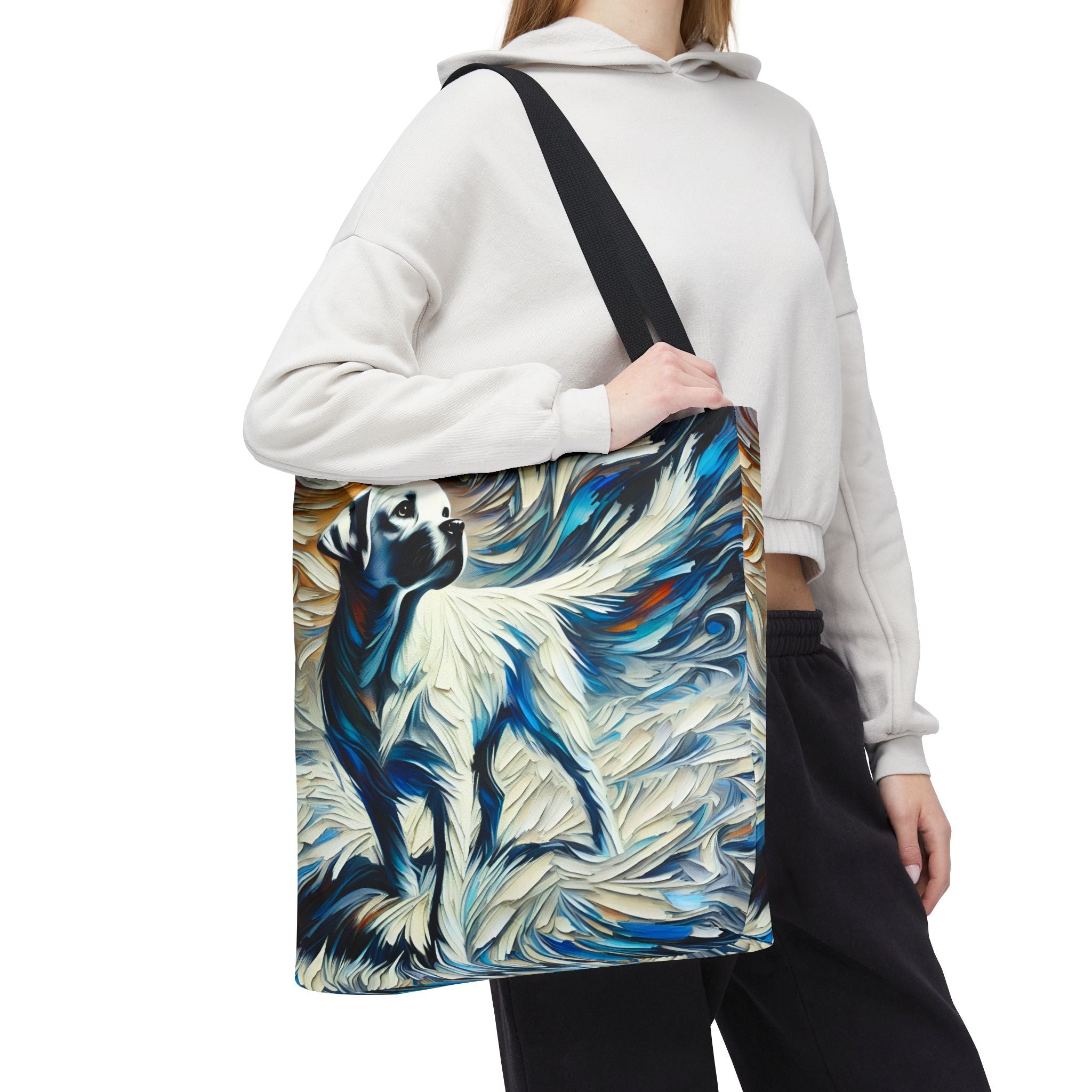 A person  carries a canvas tote bag with a black shoulder strap. The bag features a colorful abstract painting of a white Labrador retriever in blue, white, black, and beige tones.