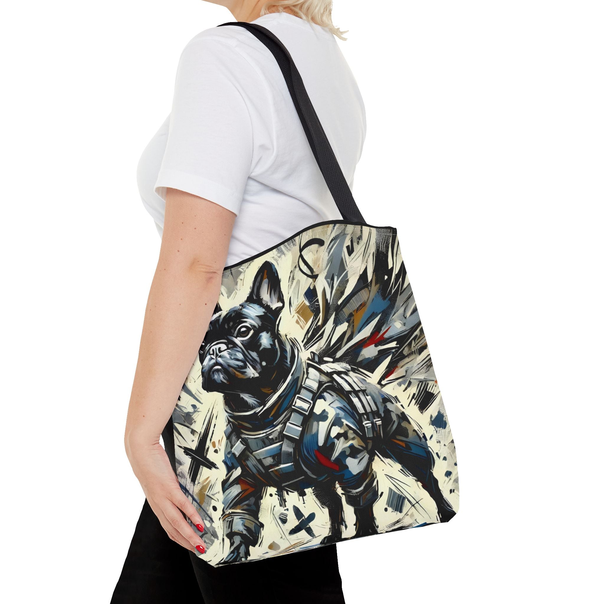 A woman wearing a white t-shirt and black pants carries a canvas tote bag with a black shoulder strap. The bag features a detailed graphic print of a black French Bulldog in tactical armor against a cream-colored background with abstract paint splatters.