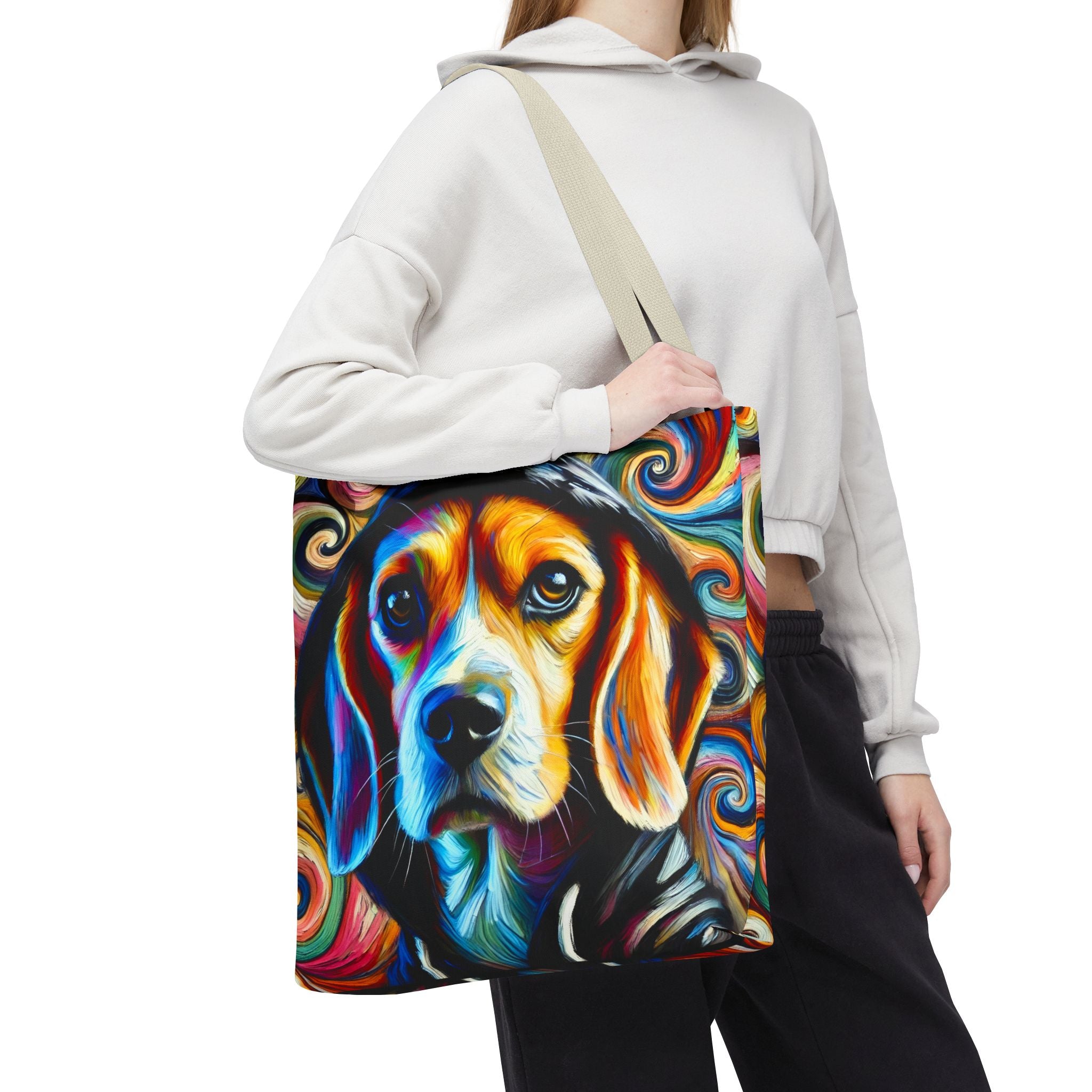 A person wearing a white cropped hoodie and black sweatpants carries a canvas tote bag over their shoulder. The bag features a vibrant, colorful abstract painting of a beagle's face with swirling paint patterns.