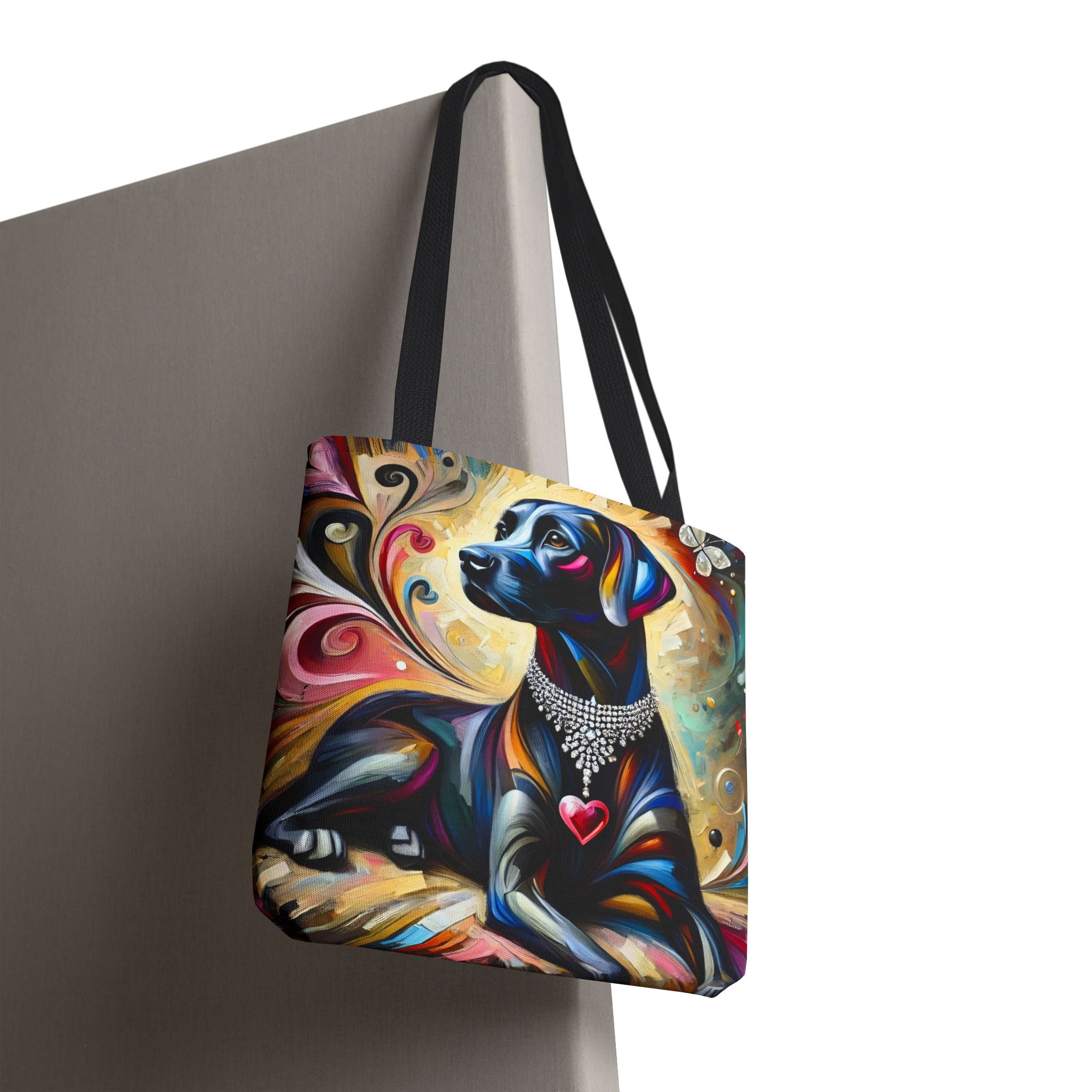 A tote bag with black shoulder straps, featuring a colorful artistic print of a black Labrador retriever wearing a silver collar and heart necklace, set against a neutral gray background.