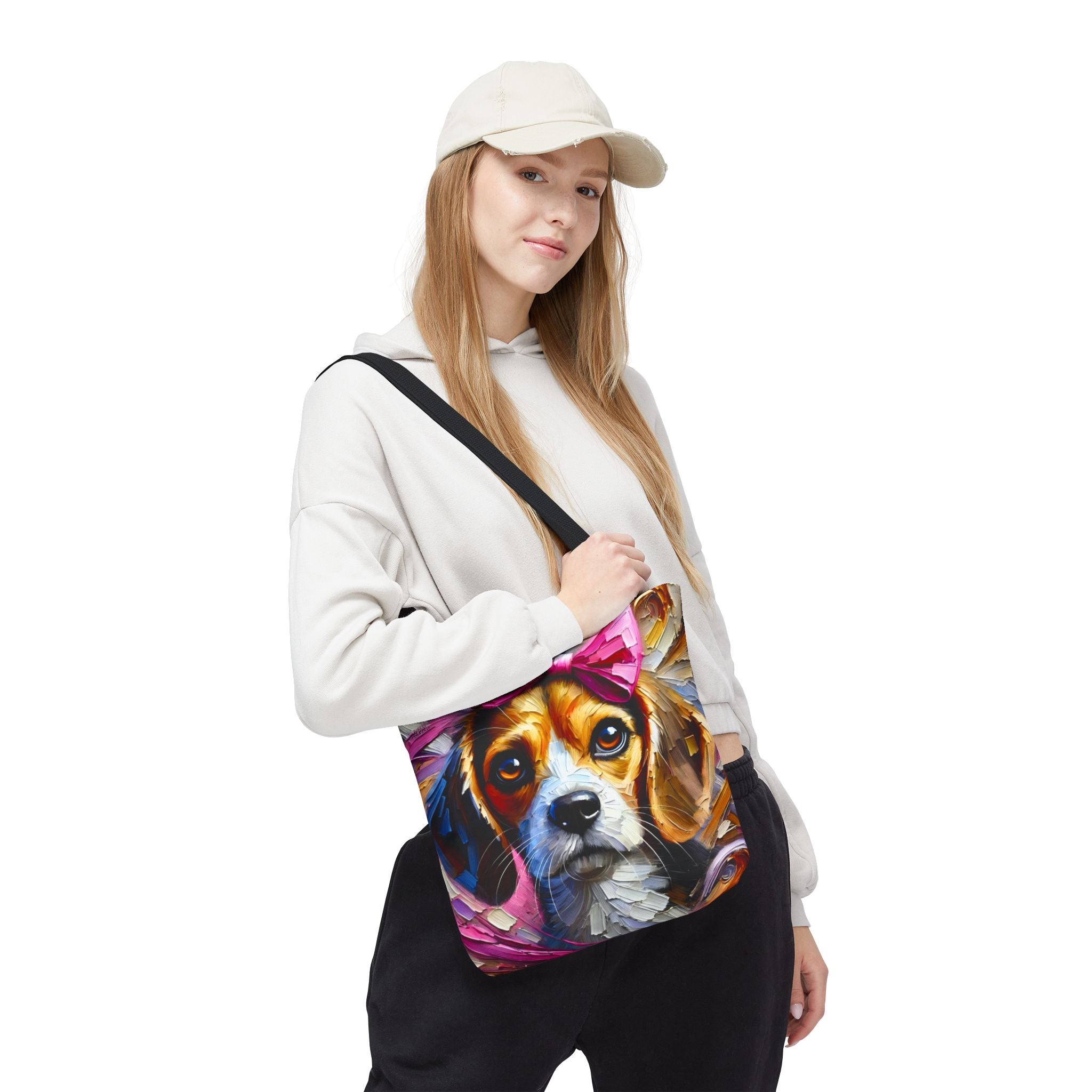 A woman wearing a beige cap, white hoodie, and black sweatpants carries a canvas tote bag with a colorful painted beagle dog print on a white background.