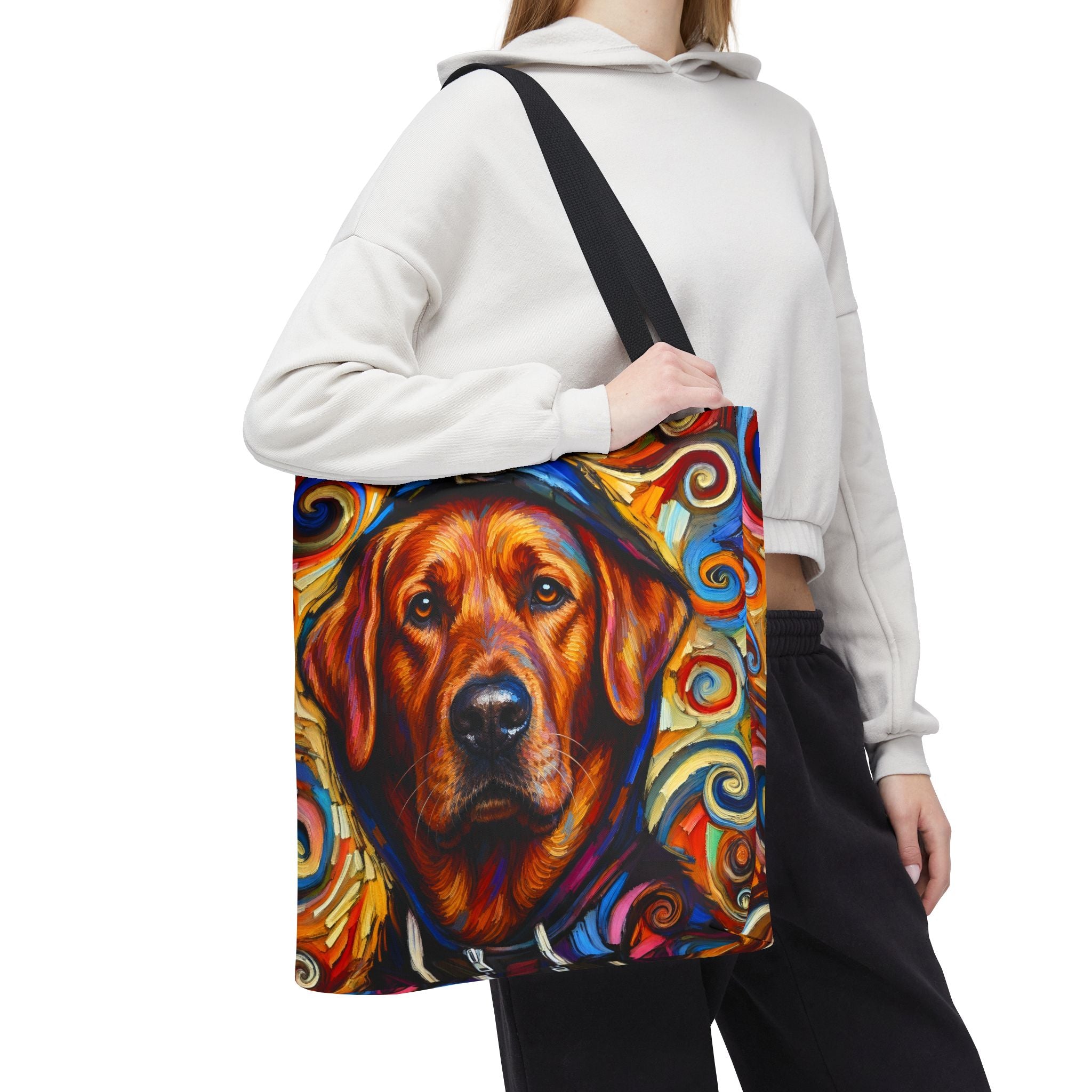 A person wearing a white cropped hoodie and black sweatpants carries a canvas tote bag with a colorful painted red fox Labrador Retriever portrait on the front. The bag has a black shoulder strap and is shown against a plain white background.