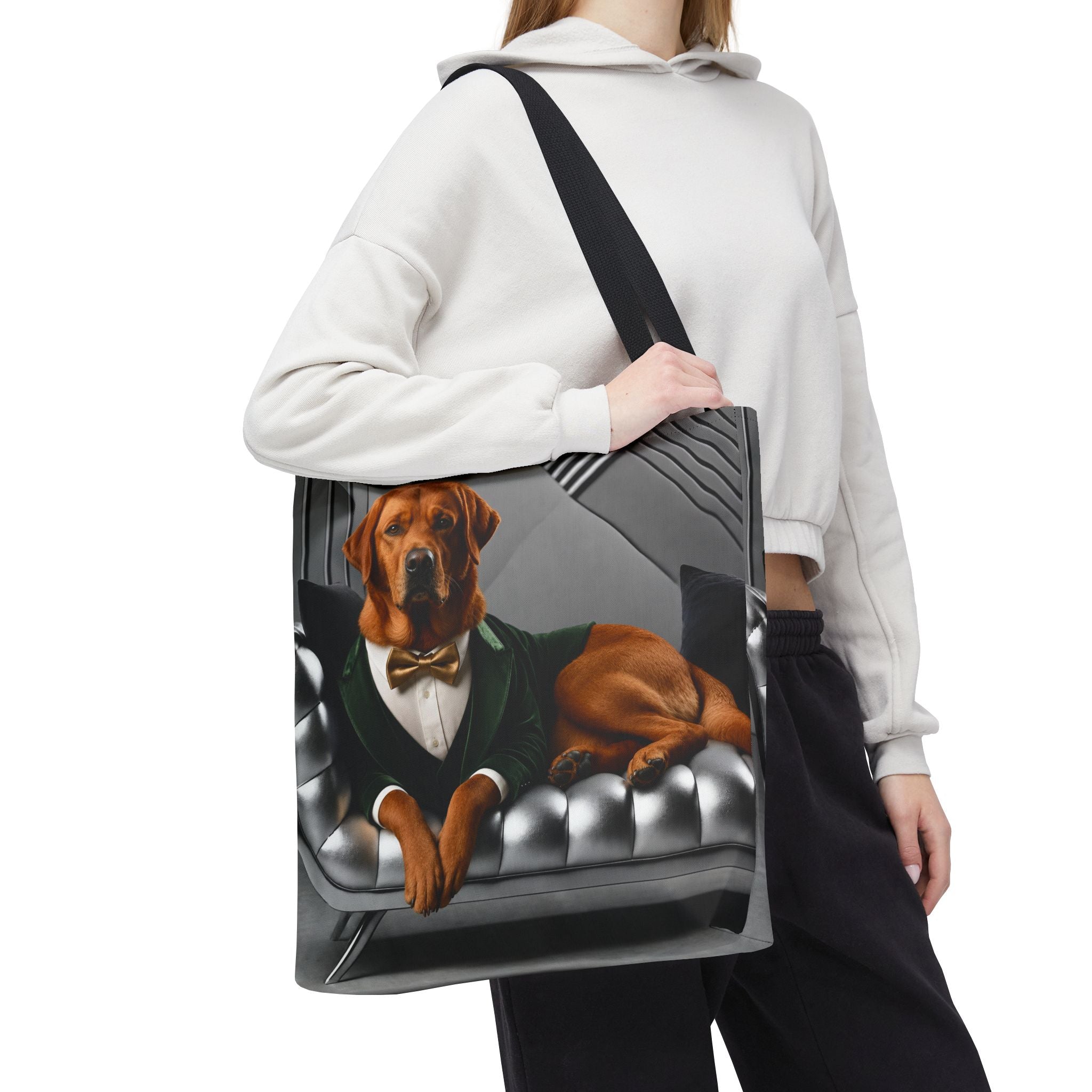 A person carries a large tote bag over their shoulder. The tote bag features a printed illustration of a fox red Labrador retriever dressed in a green suit and bow tie, lying on a tufted gray sofa.