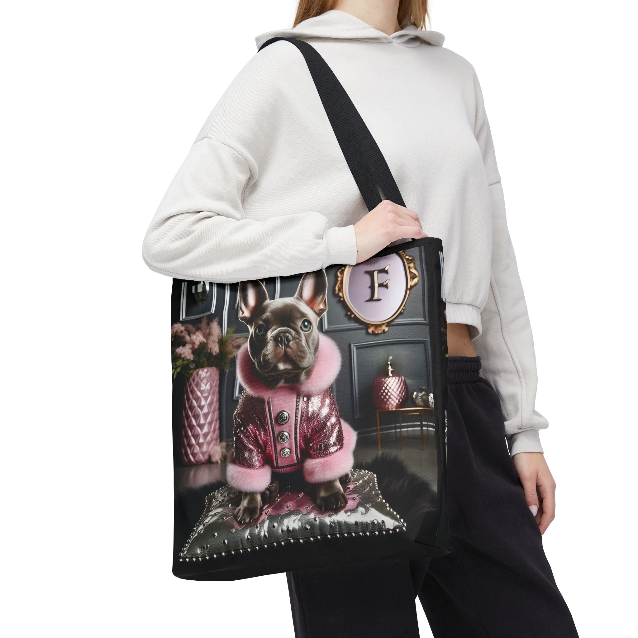 A model wearing a white cropped hoodie and black pants carries a black tote bag featuring a printed graphic of a French Bulldog in a pink jacket.