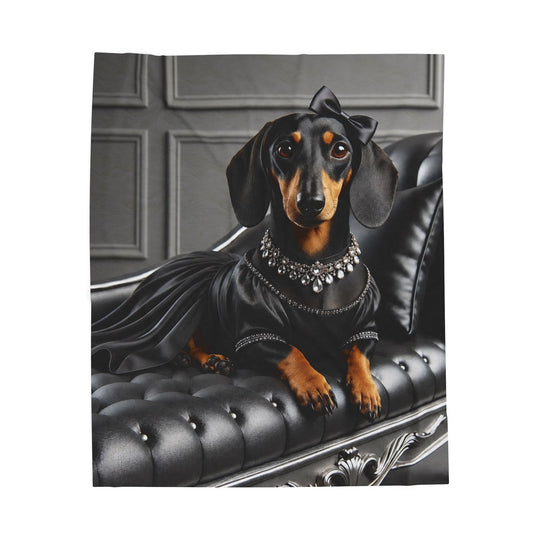 A square blanket featuring a dachshund dressed in a black satin gown with a jeweled collar and bow, posed on a black tufted chaise lounge against a gray paneled background.