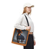 A woman wearing a white cap, white sweatshirt, and black pants carries a canvas tote bag with a brown leather-look border. The bag features a printed image of a dachshund wearing blue overalls against a dark background.