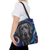 A woman wearing a white t-shirt and black pants carries a canvas tote bag featuring a painted silver Labrador retriever portrait with swirling blue, orange, and white artistic details and a black shoulder strap, against a plain white background.