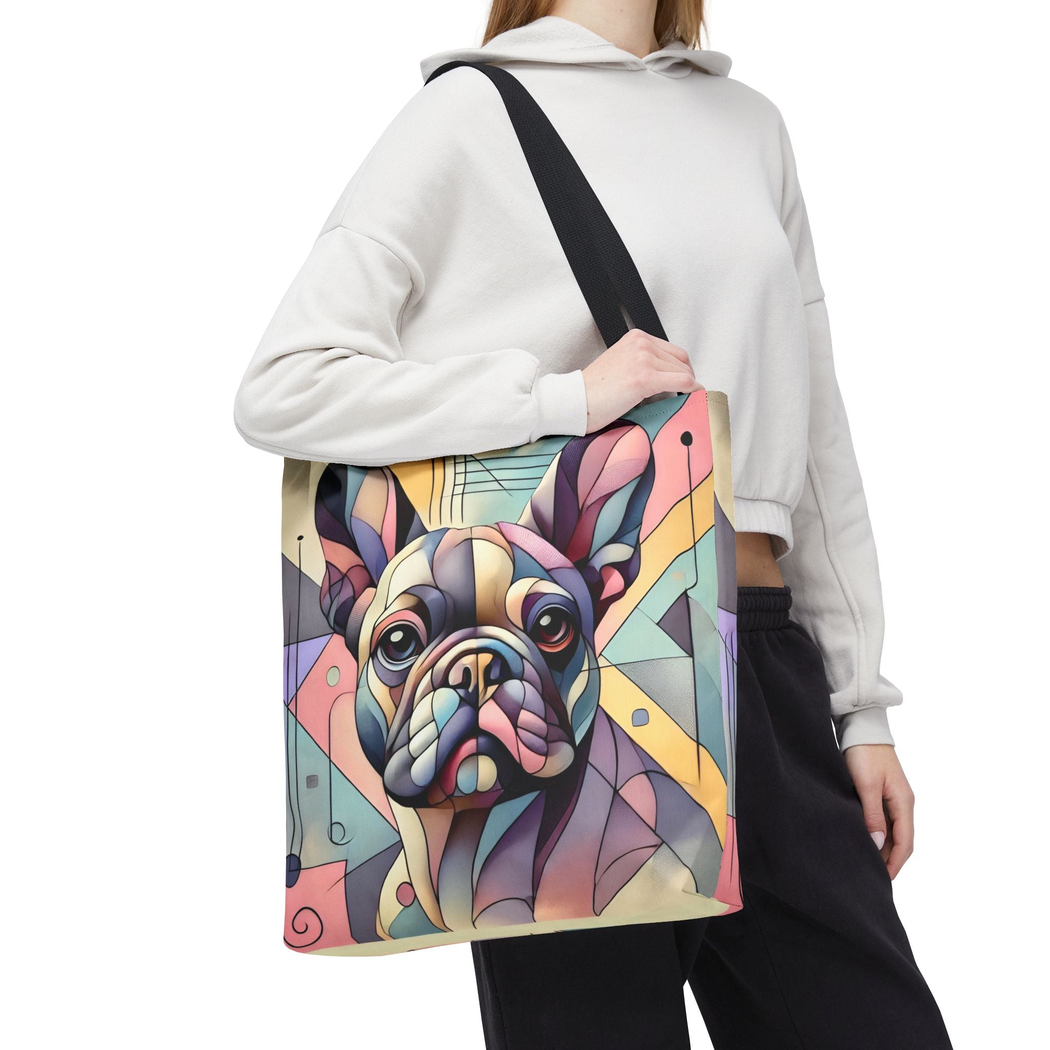 A person wearing a white cropped hoodie and black pants carries a large tote bag featuring a colorful geometric illustration of a French bulldog. The bag has a black shoulder strap and is shown against a plain white background.